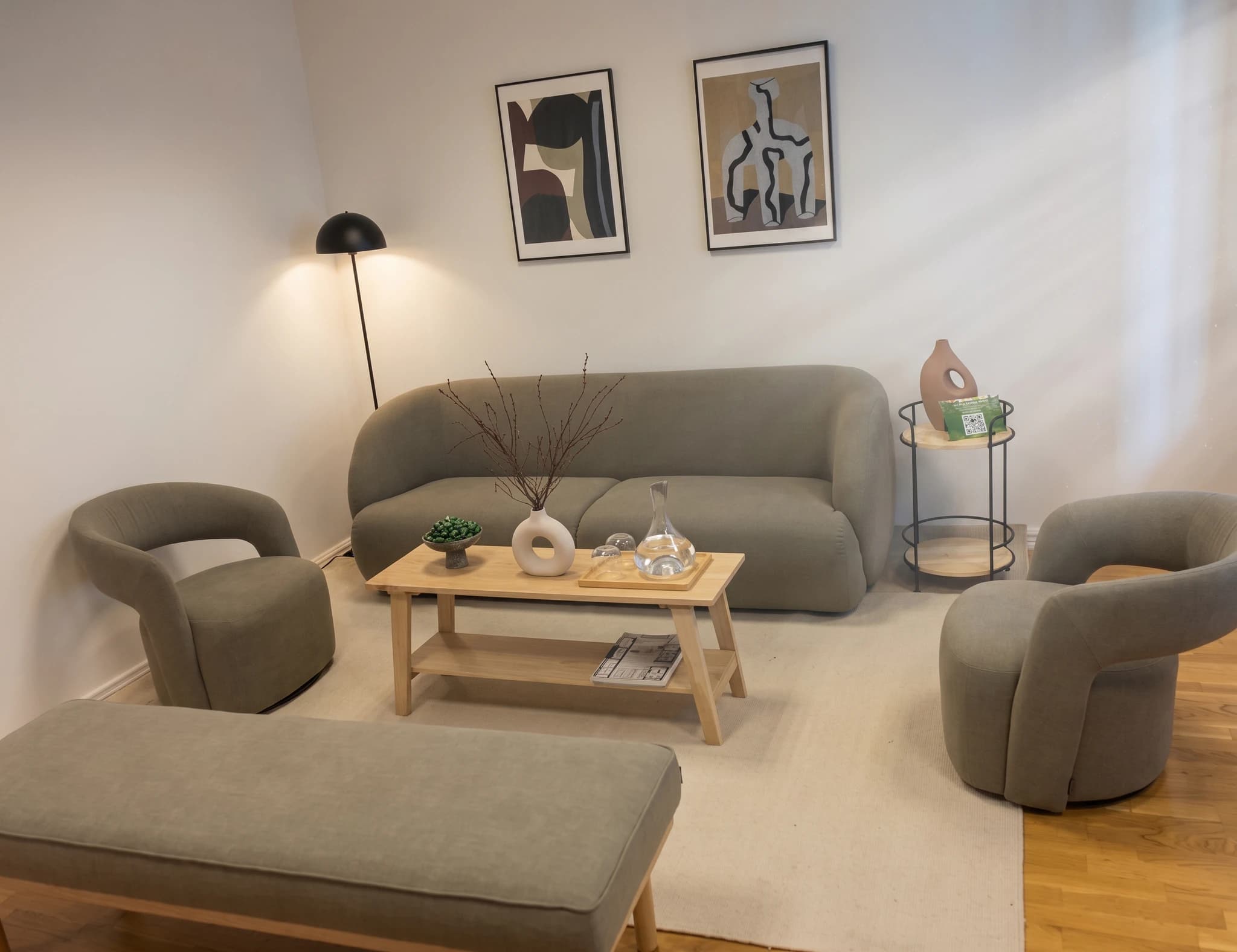 Modern inredd vardagsrum med grå soffa, fåtöljer, soffbord och konst på väggen.
