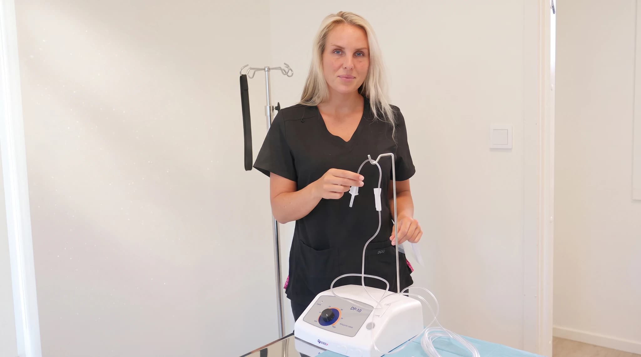 En sjuksköterska i mörkblå scrubsdress visar upp en IV-infusionspump och slangar.