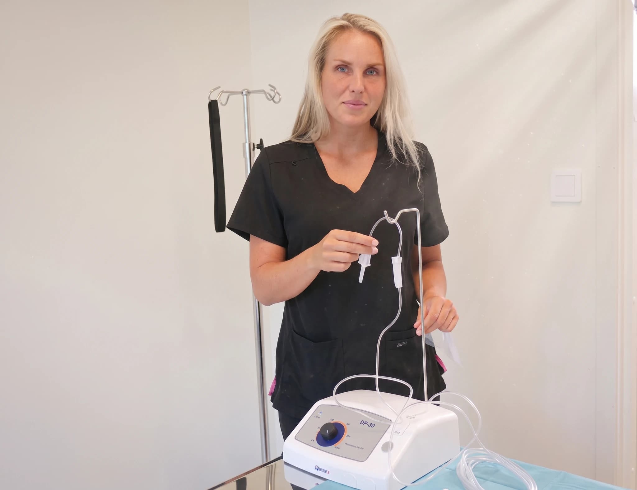 Sjuksköterska med droppställning, infusionspump och droppslangar i behandlingsrum.