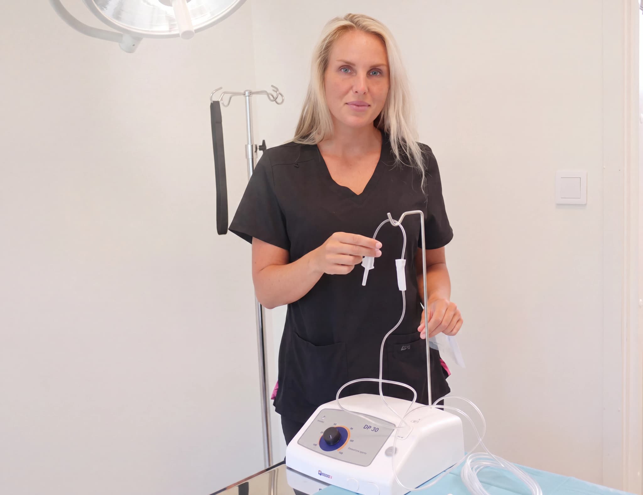 Sjuksköterska håller upp infusionsslang som ansluter till en infusionspump i ett behandlingsrum.
