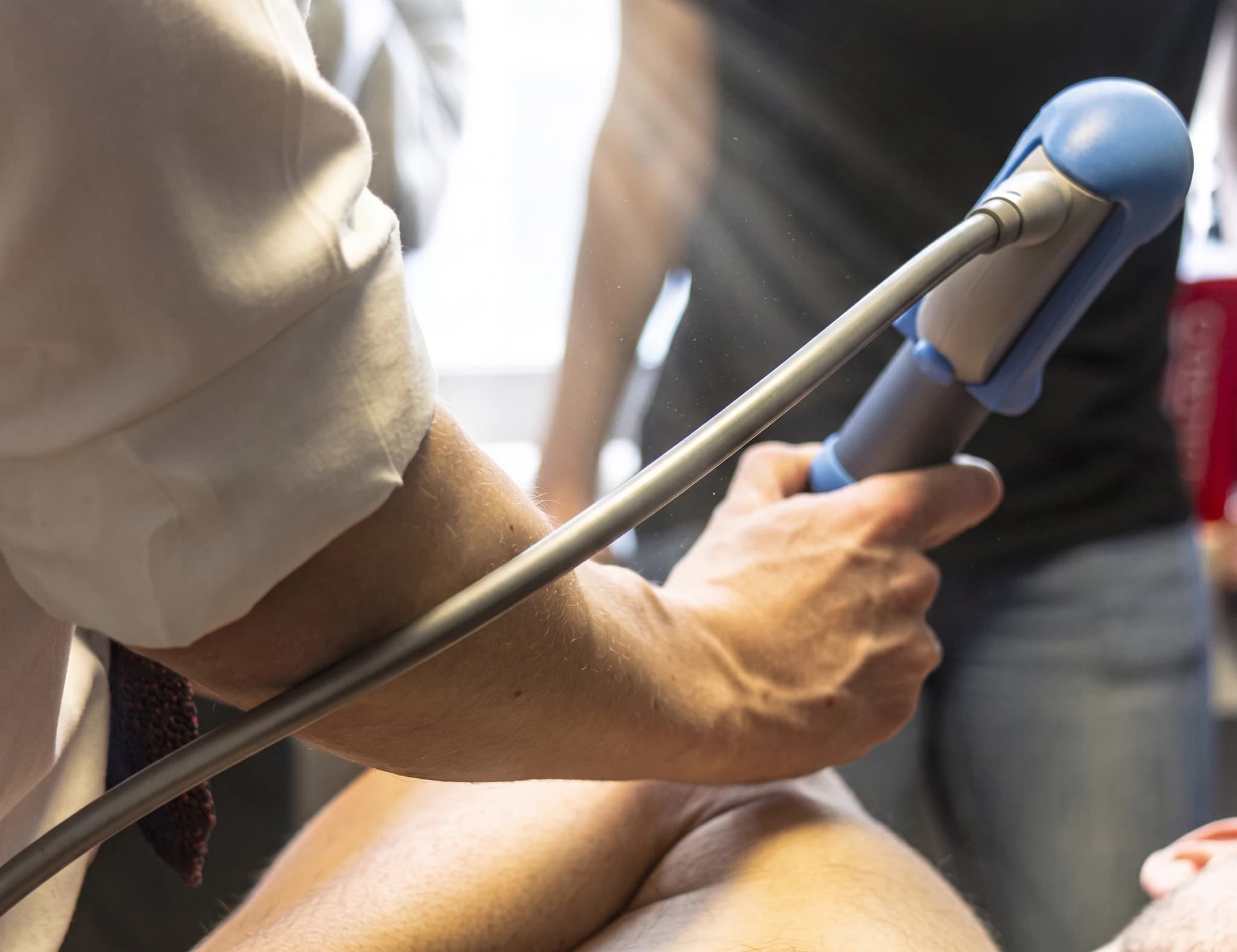 En fysioterapeut använder en chockvågsbehandlingsapparat på en patients ben.