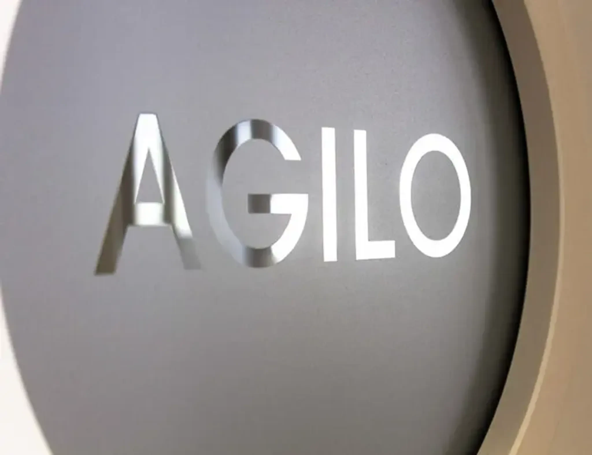 Agilo-företagets logotyp med texten AGILO i gråa bokstäver på en rundad bakgrund.