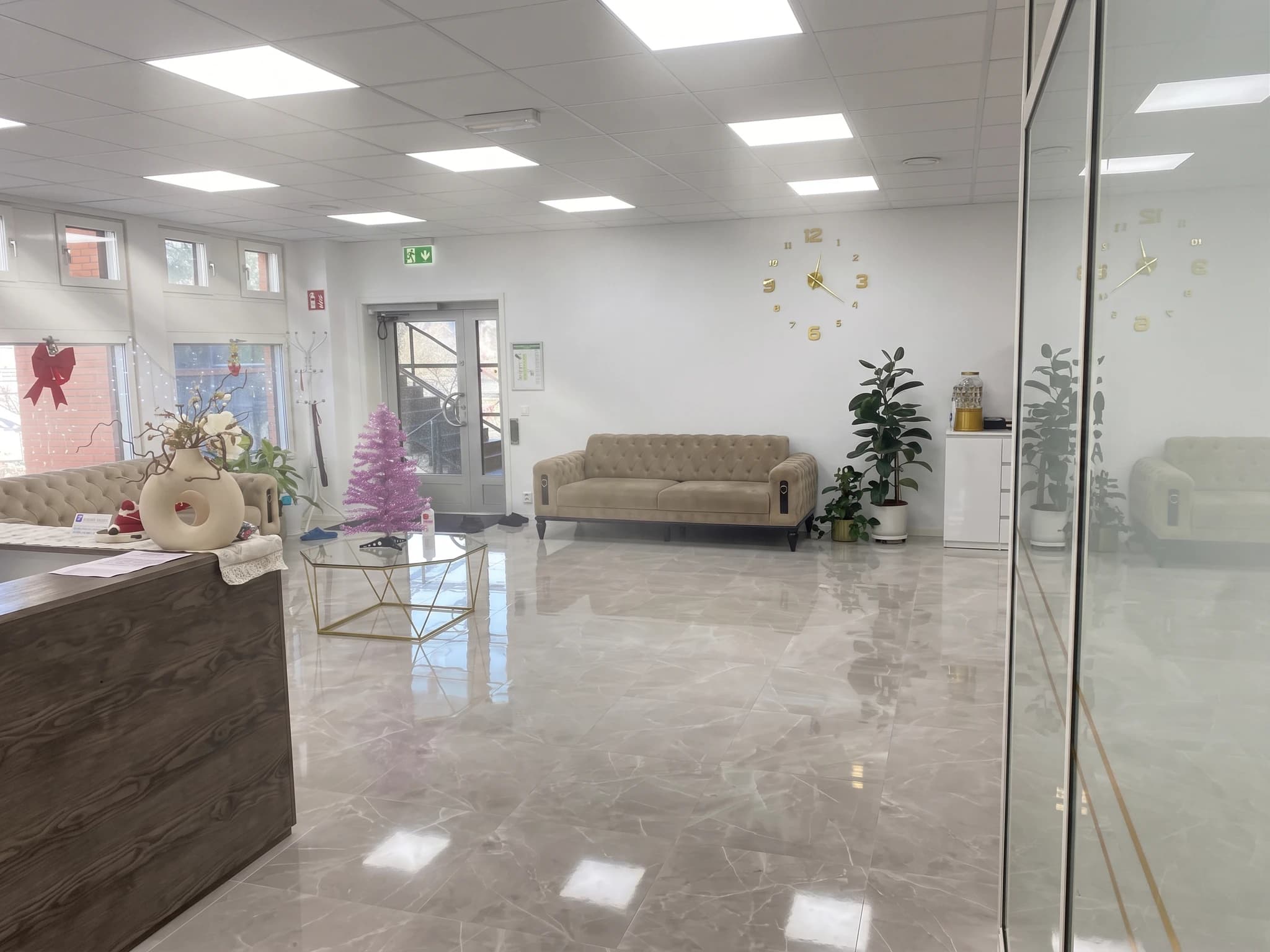 Ljus och modern receptions- och väntrumsdel med juldekorationer, inklusive ett rosa julgransliknande träd och en röd rosett.