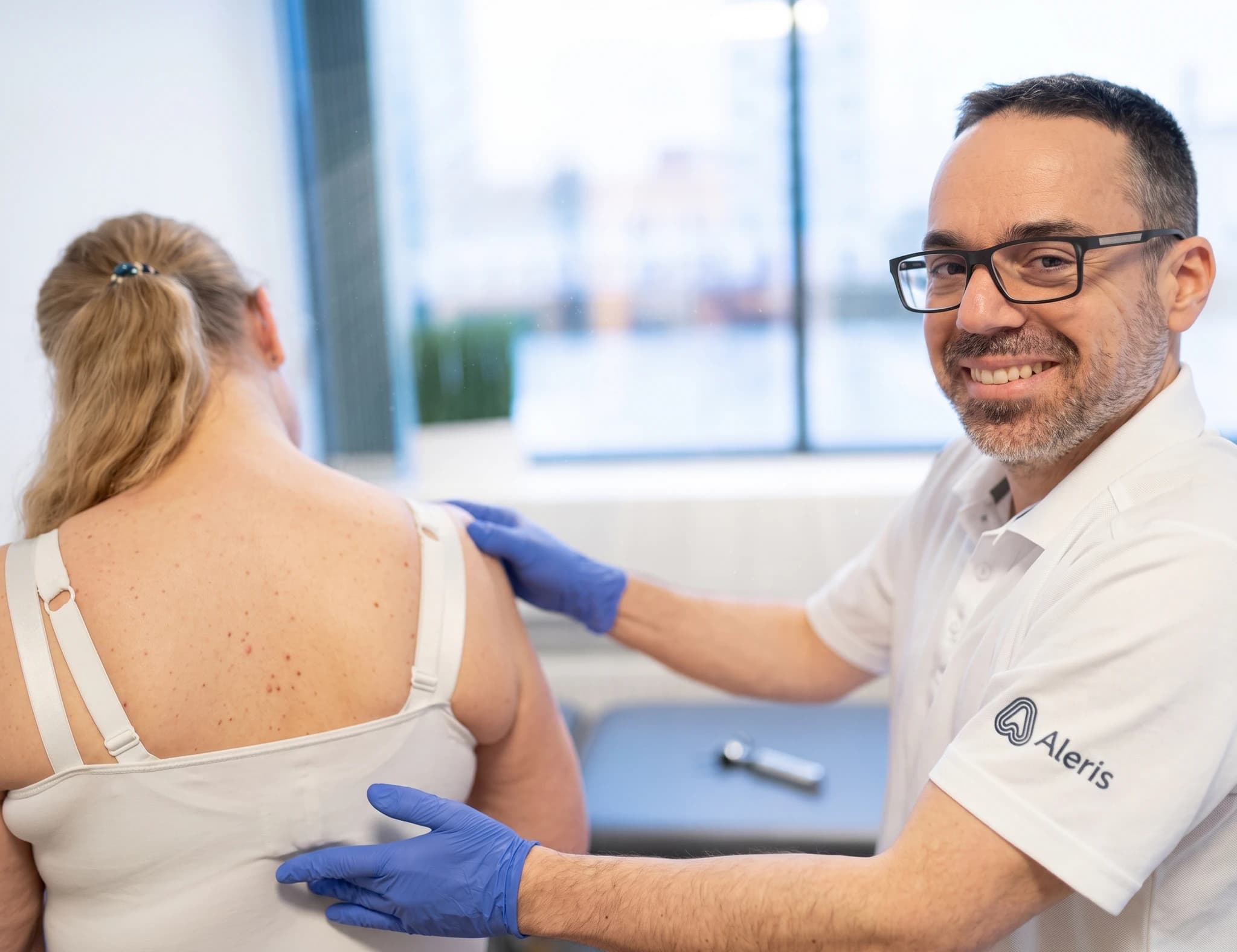 Fysioterapeut med blå handskar undersöker en patients rygg och axel.