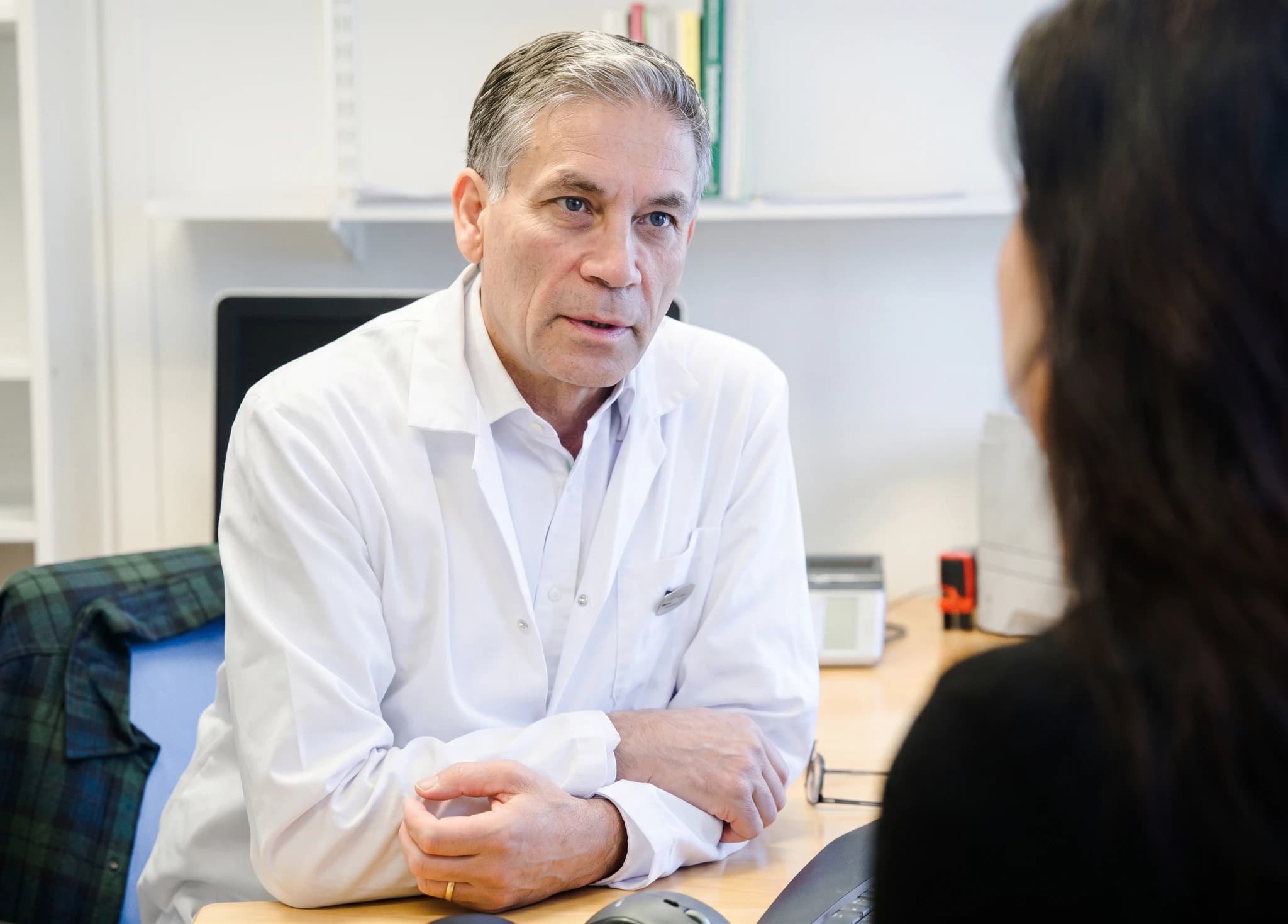 Manlig läkare i vit rock pratar med en patient i ett kontor.