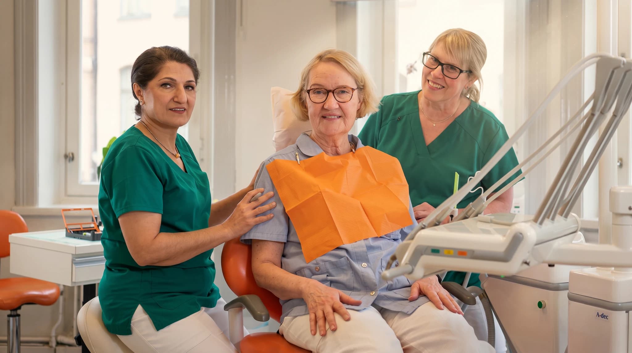 Två tandvårdspersonal står bakom en patient som sitter i en tandläkarstol.