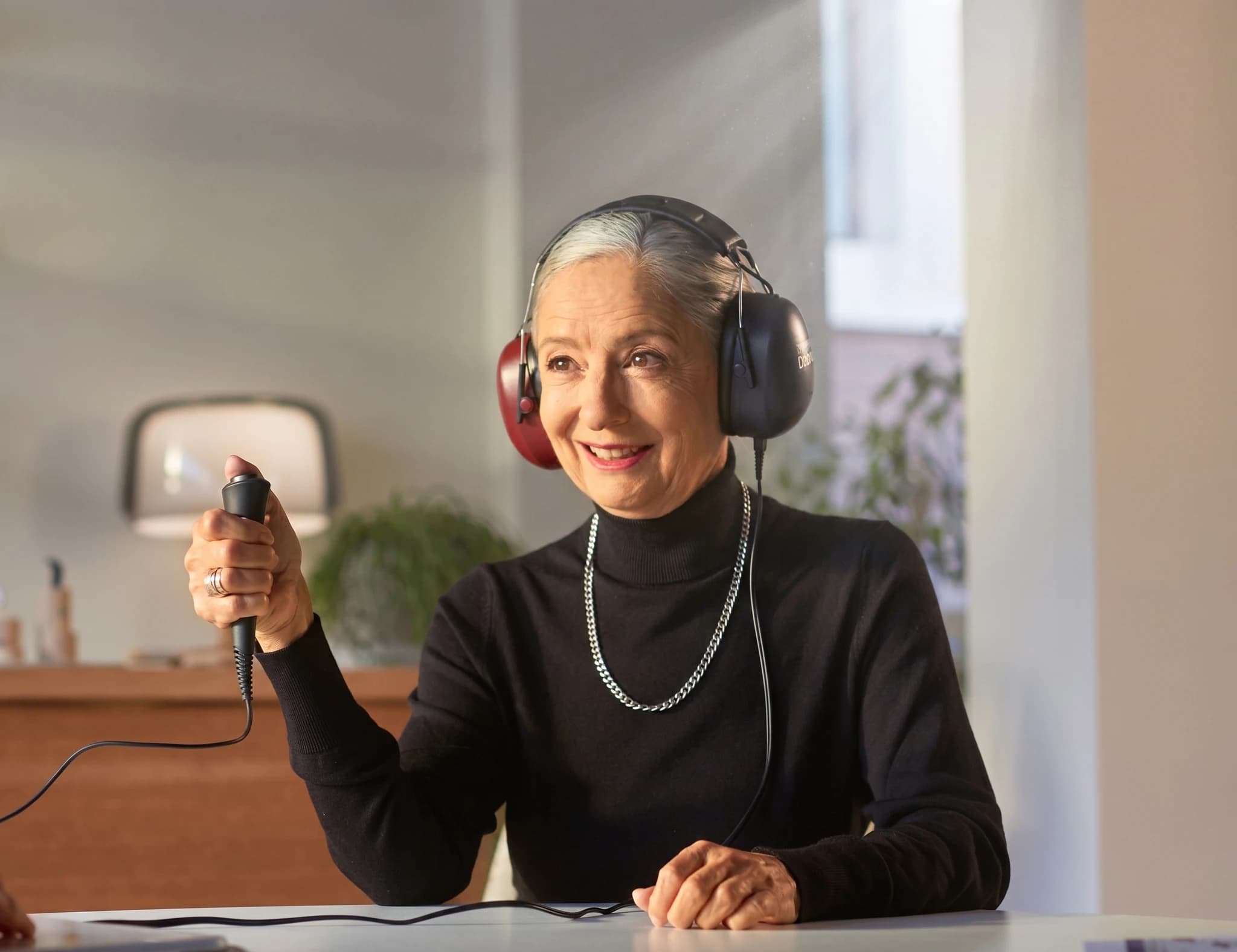 Äldre kvinna med hörlurar och mikrofon kopplad till en audiometer under ett hörseltest.