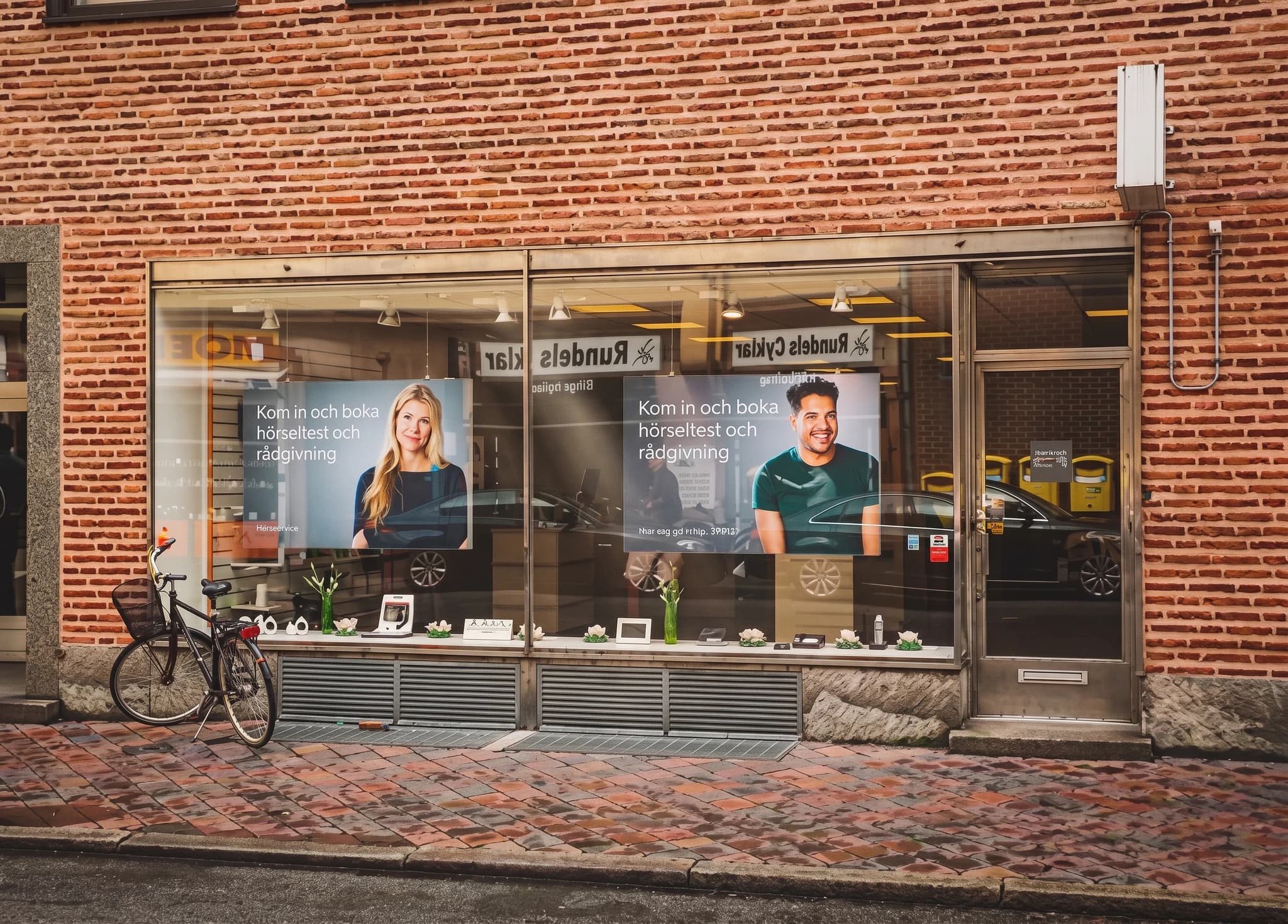 En skyltfönsterdisplay med två affischer som visar personer och text, framför en tegelbyggnad.