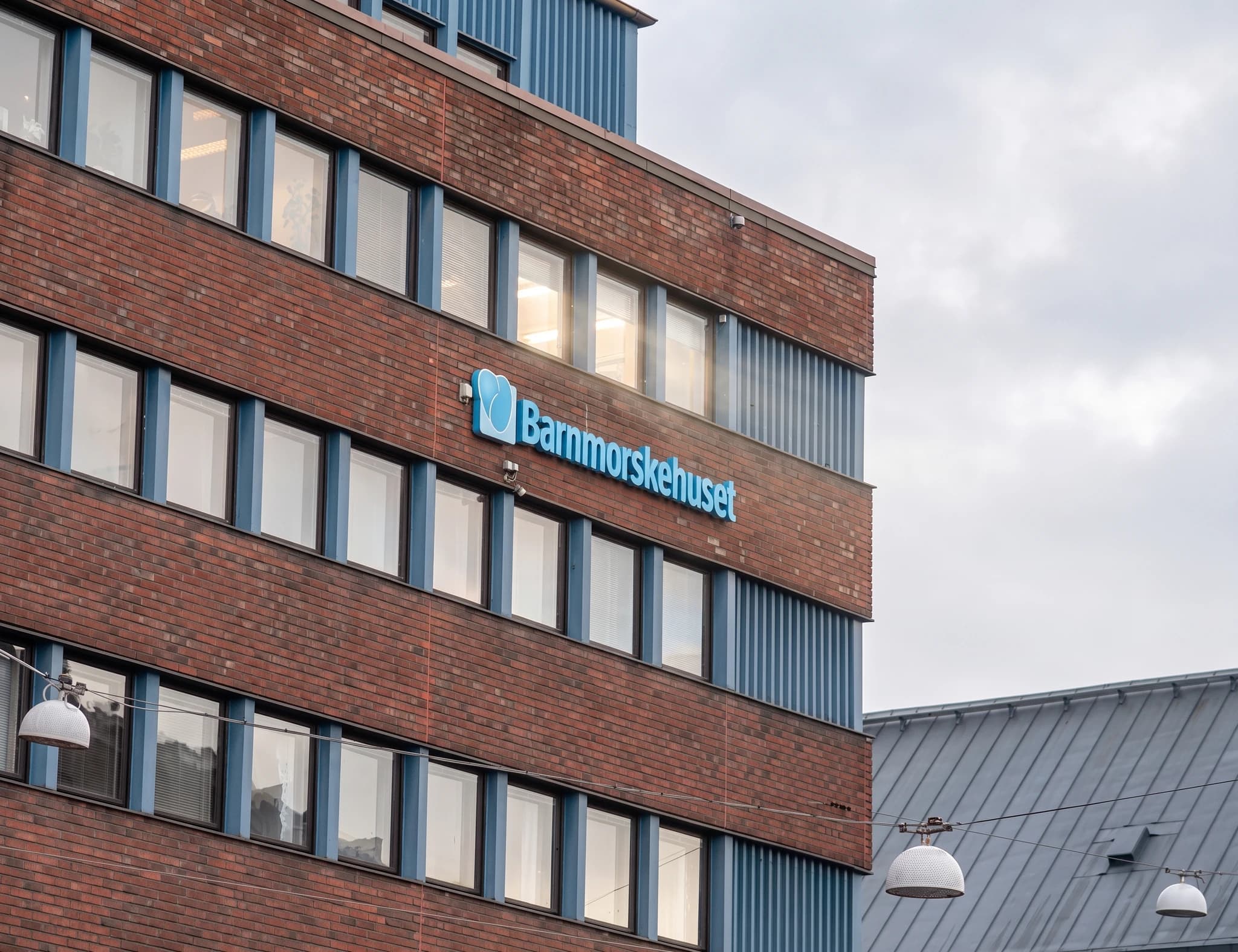 Barnmorskehuset-logotyp i blått lysande text med en symbol på en tegelbyggnad.