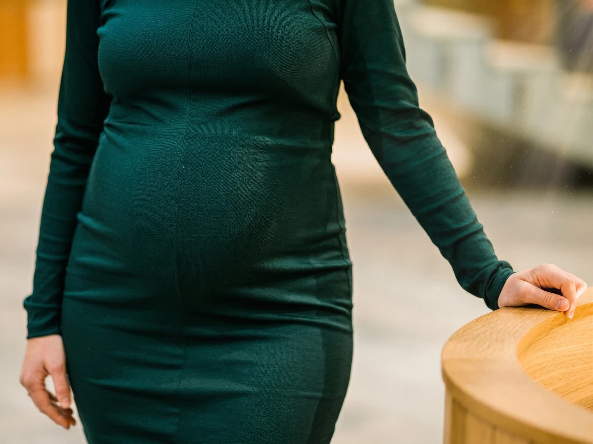 Gravid kvinna i en mörkgrön klänning som lutar sig mot en rund träyta.