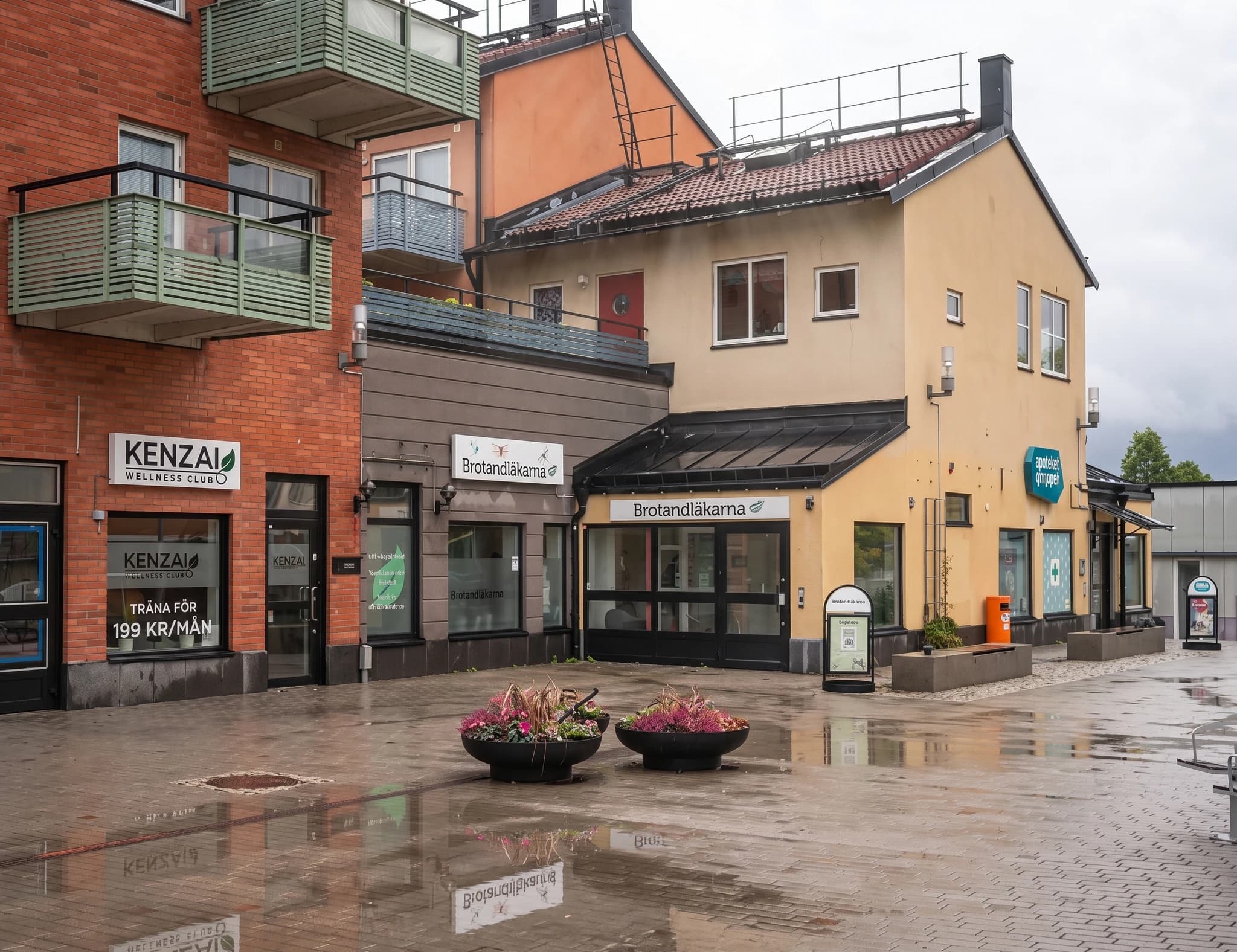 Fasad med flera butiker och lägenheter, ett tandläkar center, en wellness klubb och en liten fontän i förgrunden
