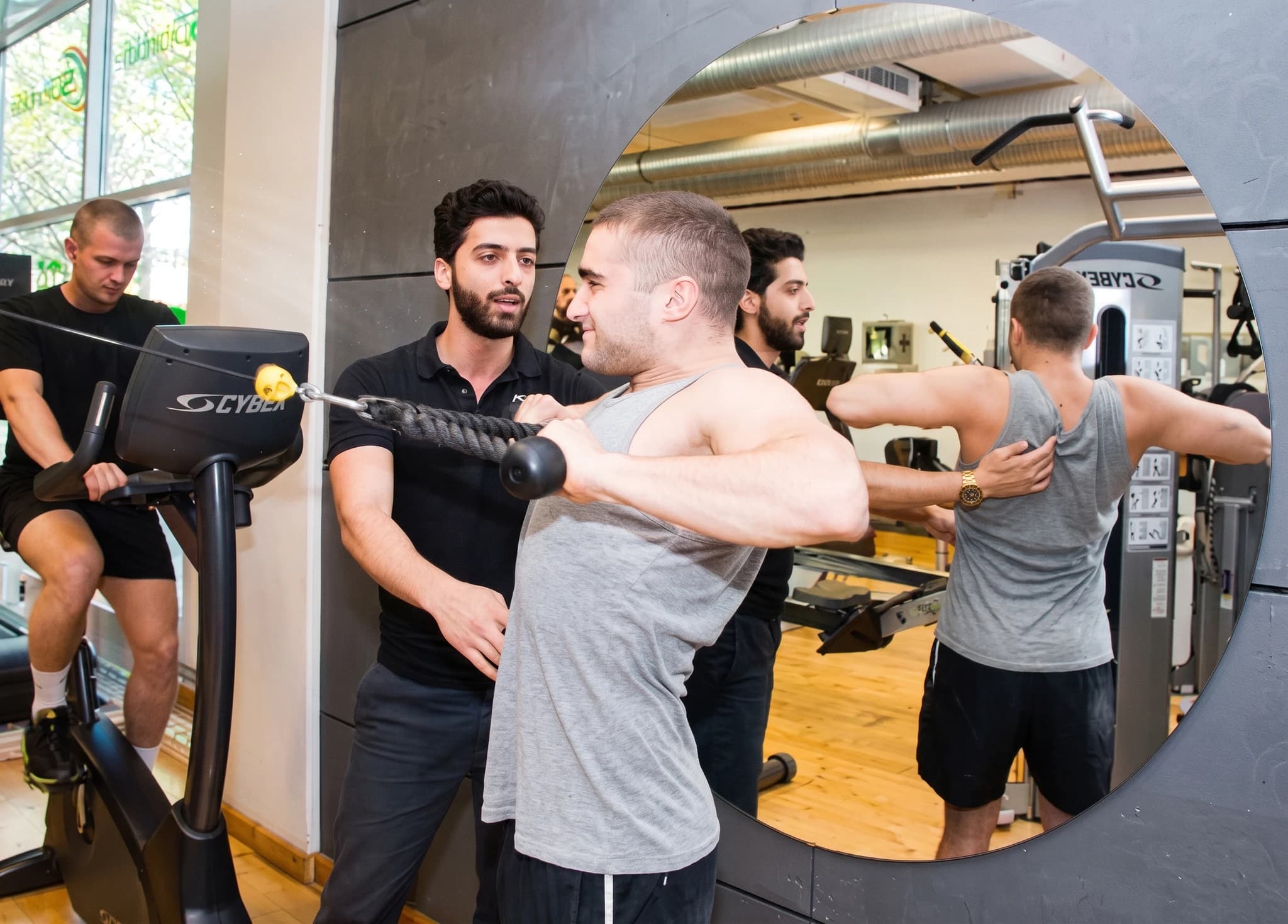 En personassistent hjälper en man att utföra en roddövning med kabelmaskin på gymmet.