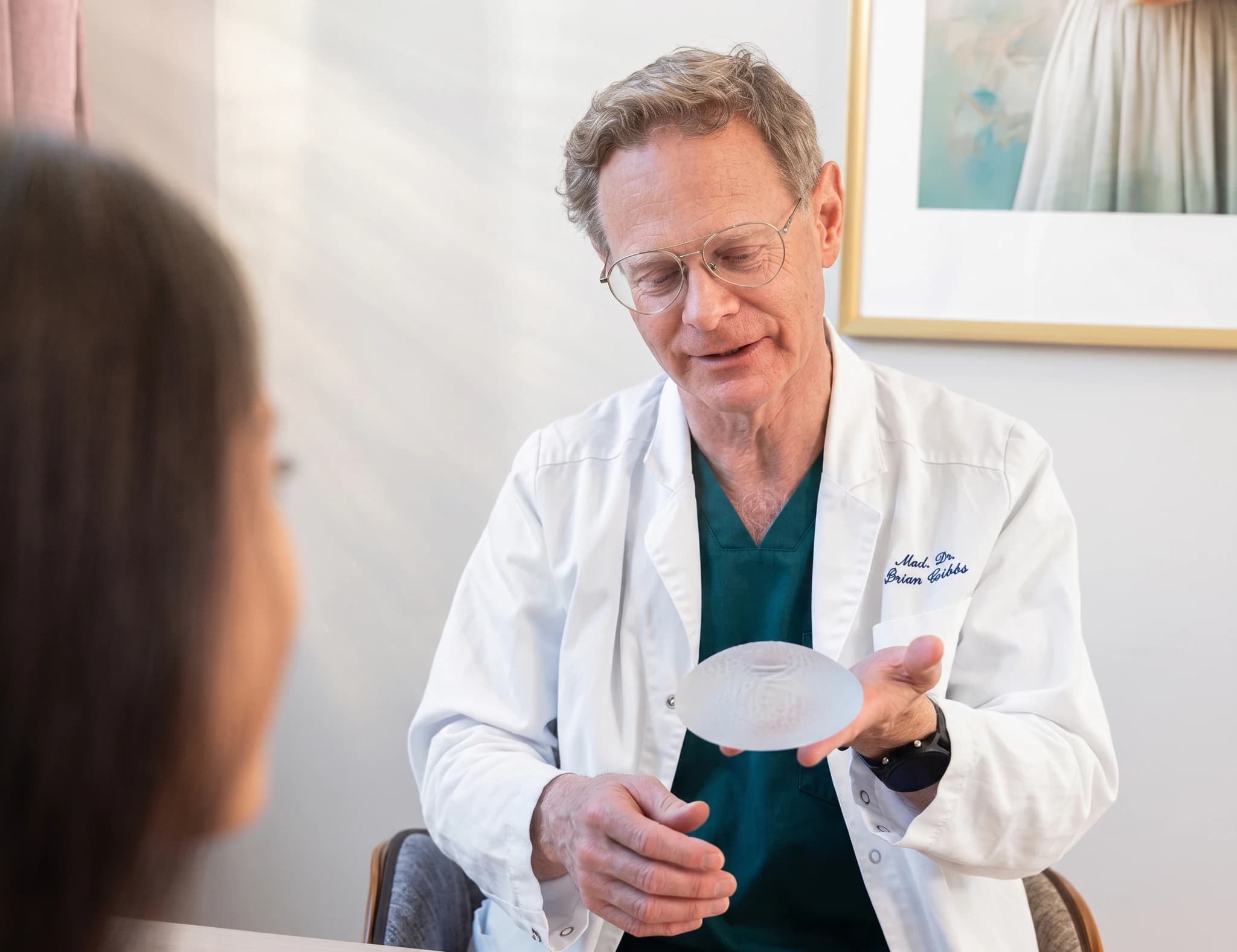 Läkare i vit rock visar ett bröstimplantat för en patient under en konsultation.