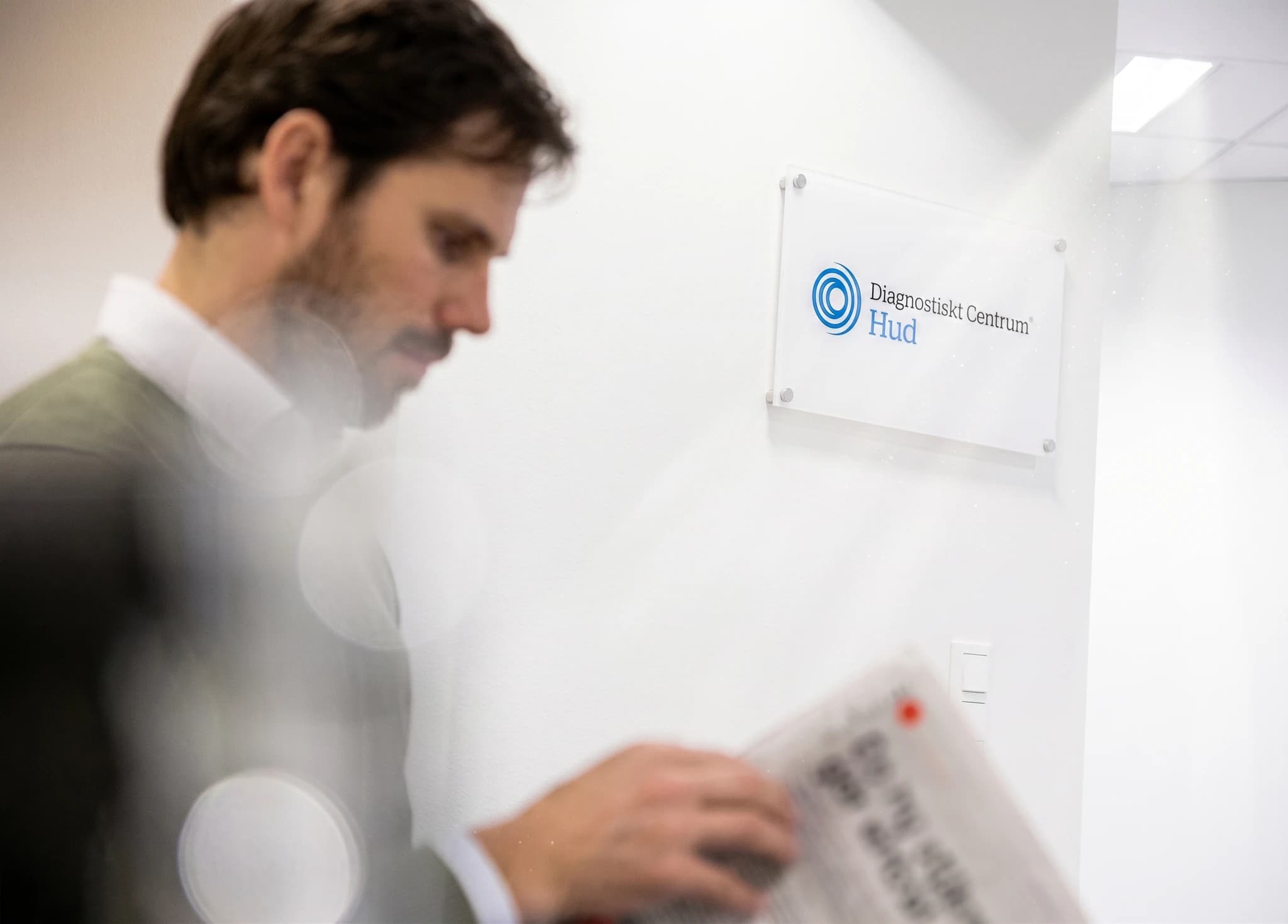 Man i kostym som läser en tidning framför en väggskylt för "Diagnostiskt Centrum Hud".