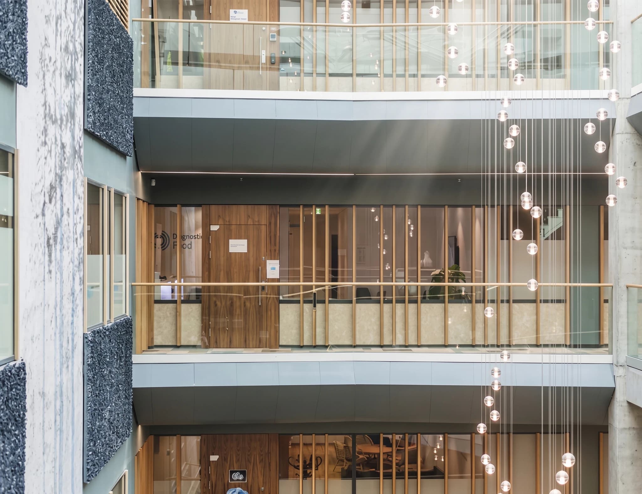 Interiörbild av ett modernt atrium med flera våningar, glasräcken och hängande ljusinstallationer.