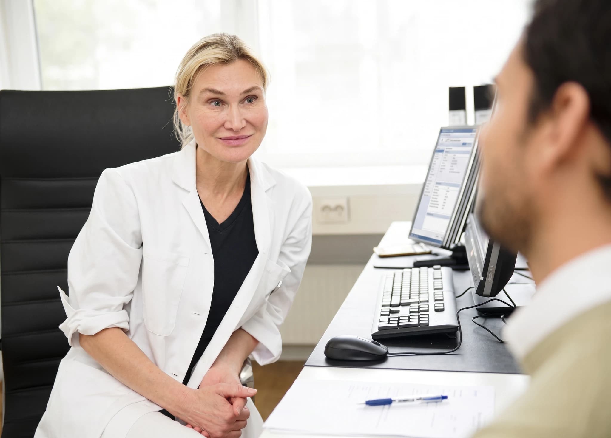 Läkare i vit rock sitter och pratar med en patient i ett klinikkontor.
