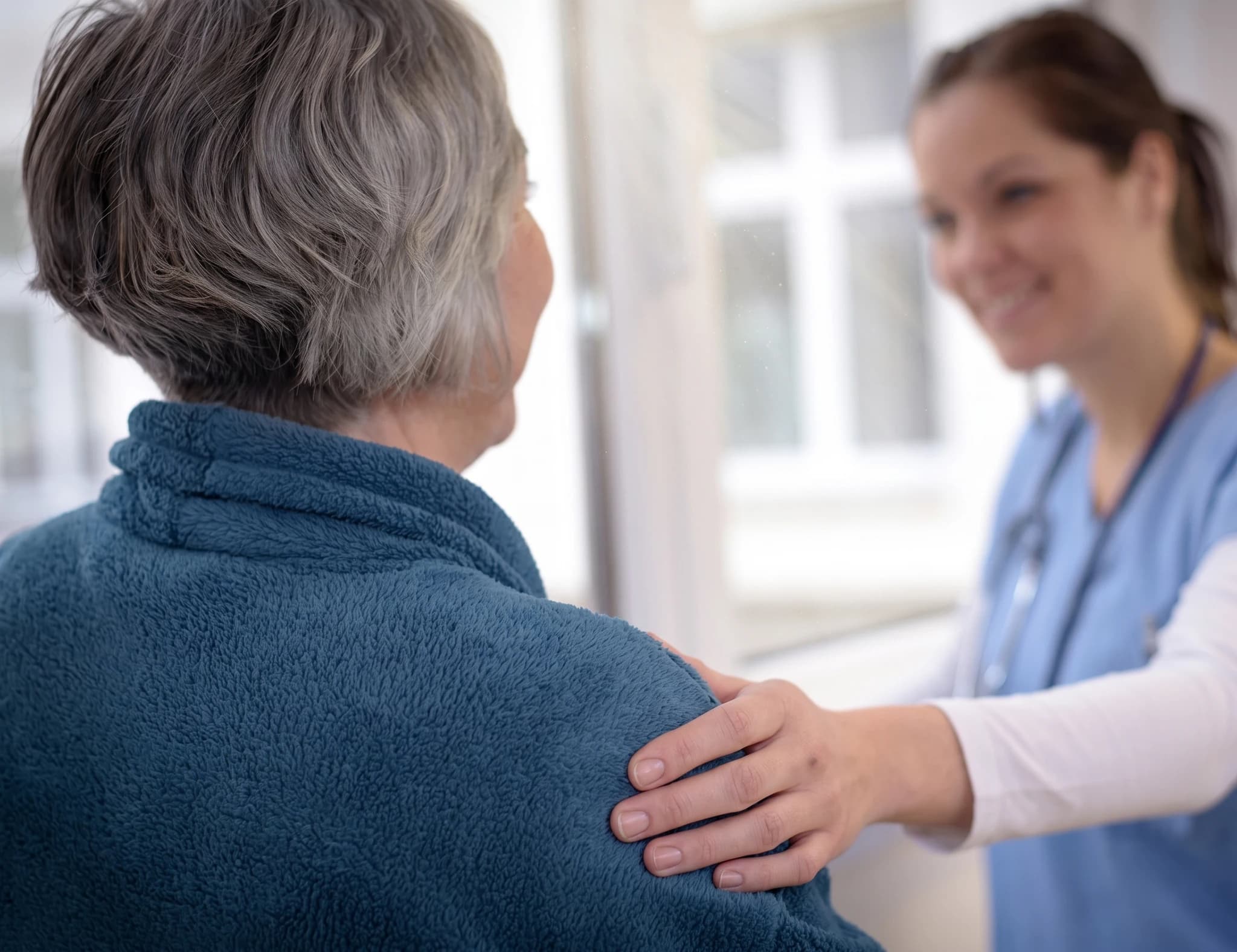 Sjuksköterska lägger en tröstande hand på en äldre patients axel.