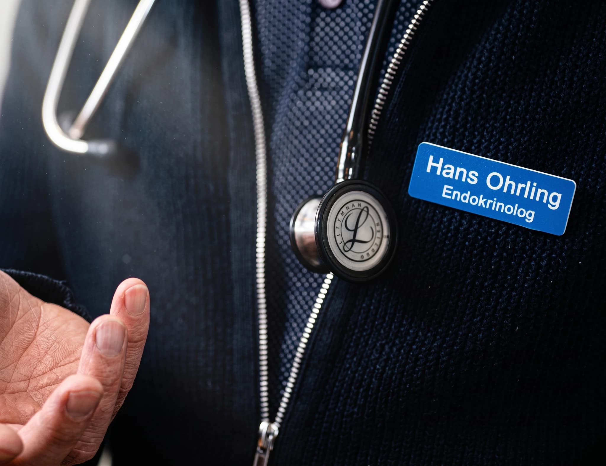 Närbild på en läkares namnskylt som visar "Hans Ohrling Endokrinolog" och ett stetoskop som hänger över kläderna.