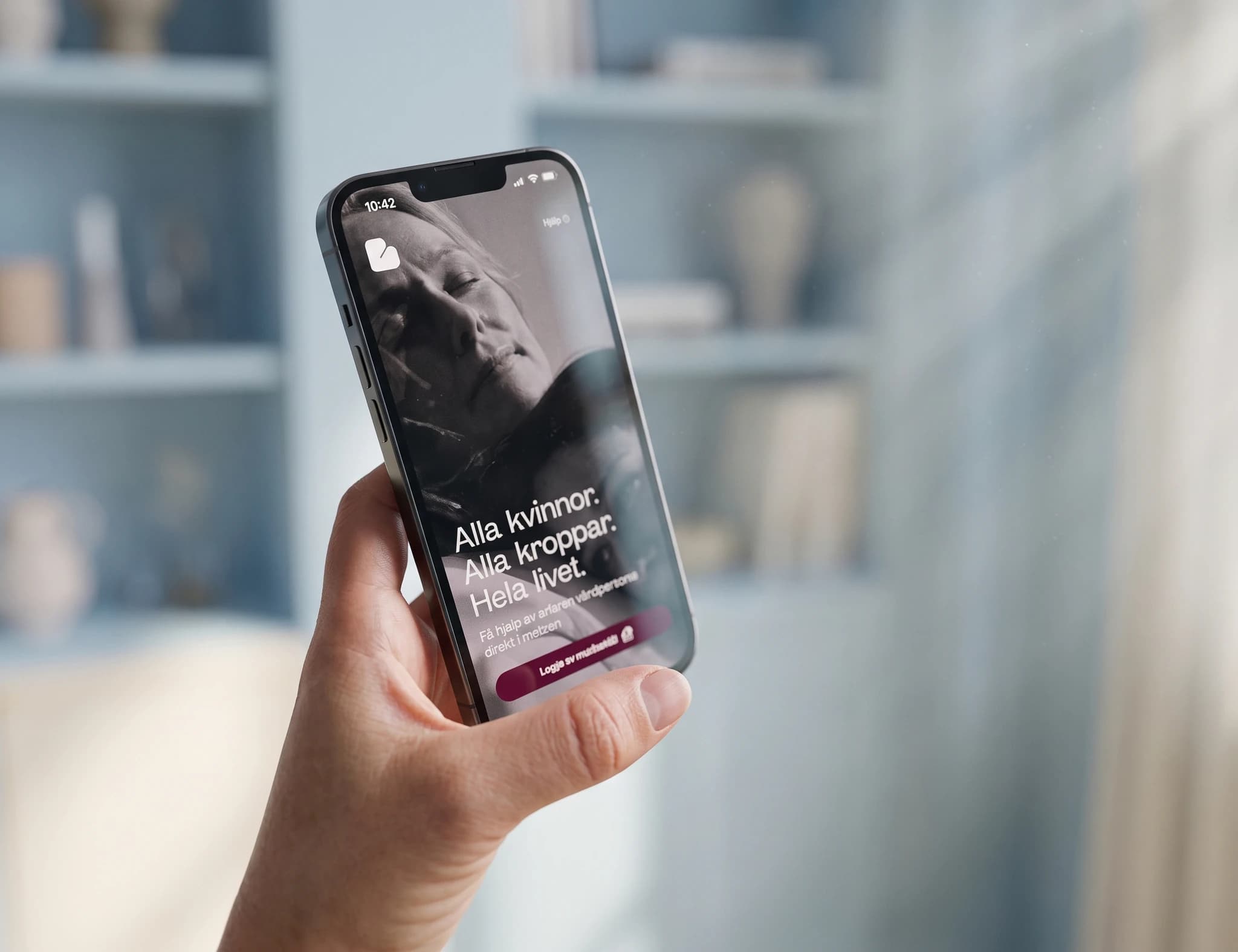 En person håller en smartphone som visar en app med texten 'Alla kvinnor. Alla kroppar. Hela livet.'
