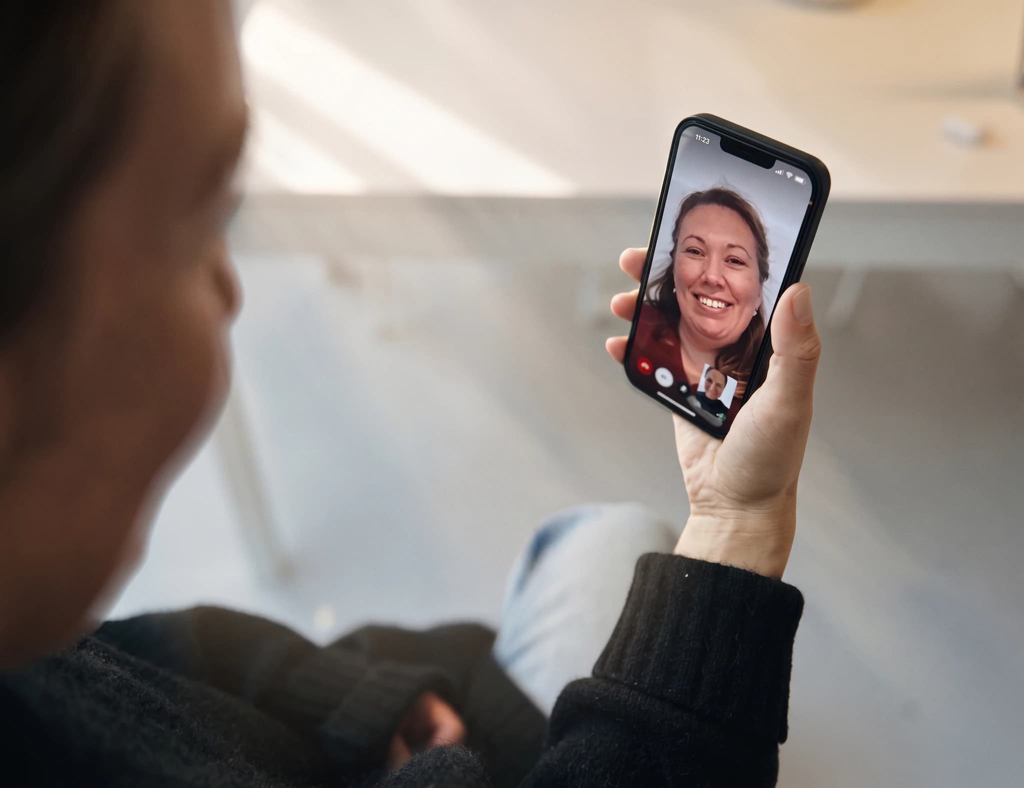 Person som håller upp en smartphone för ett videosamtal med en kvinna som ler mot kameran.