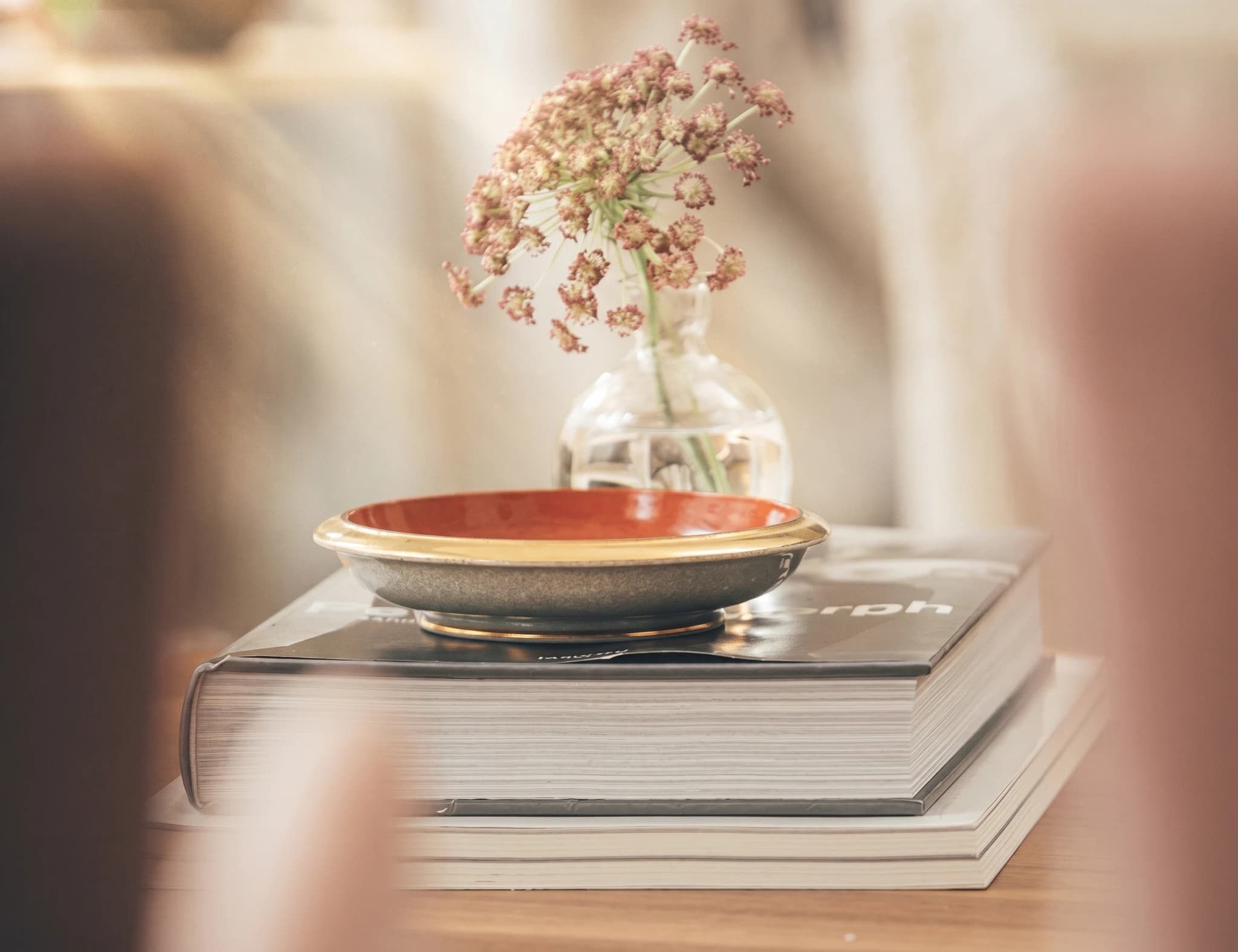 Stillbild med en stapel böcker och en glasvas med en bukett av torkade blommor ovanpå.