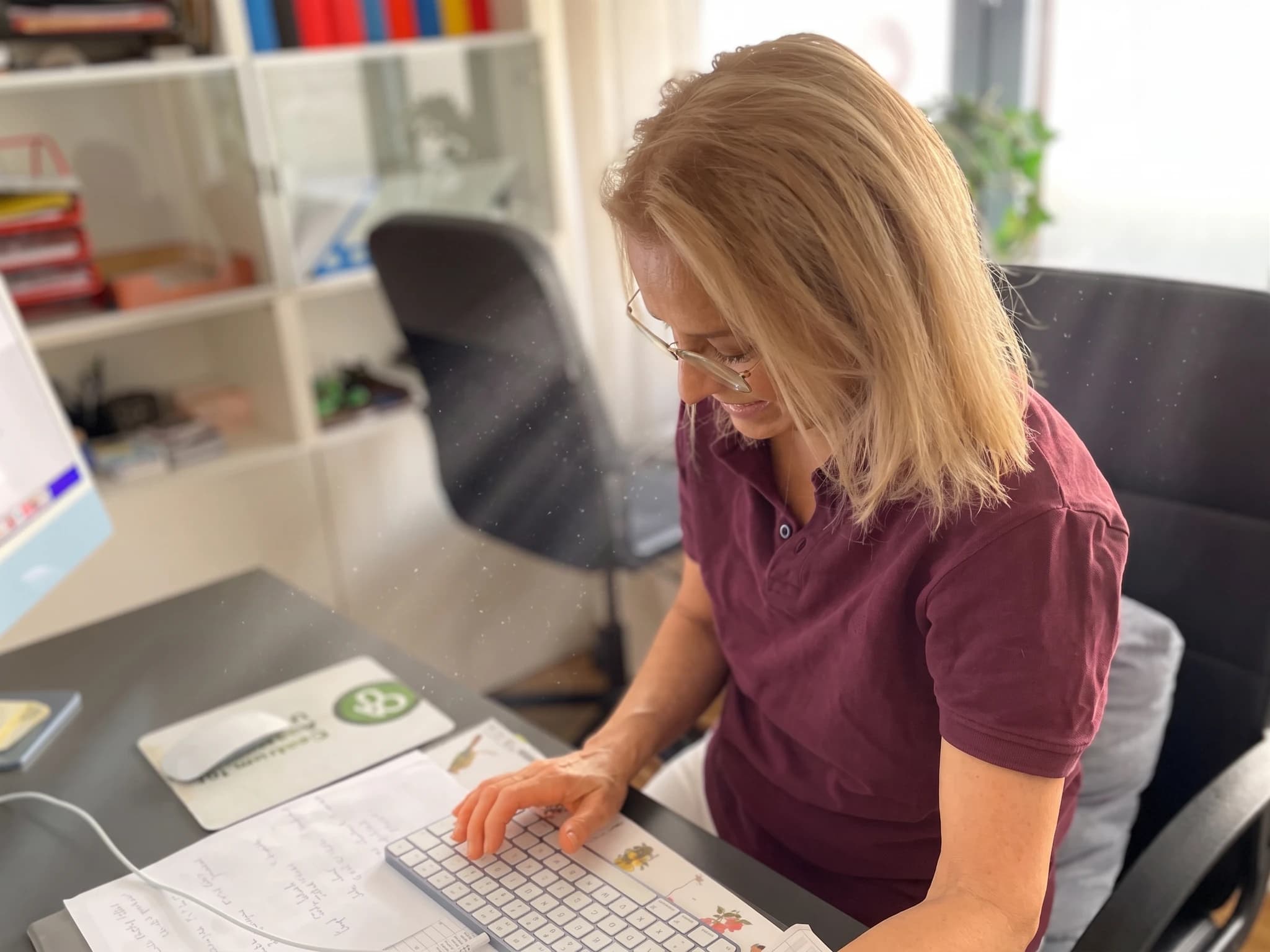 Kvinna med blont hår som sitter vid ett skrivbord och arbetar på en dator.