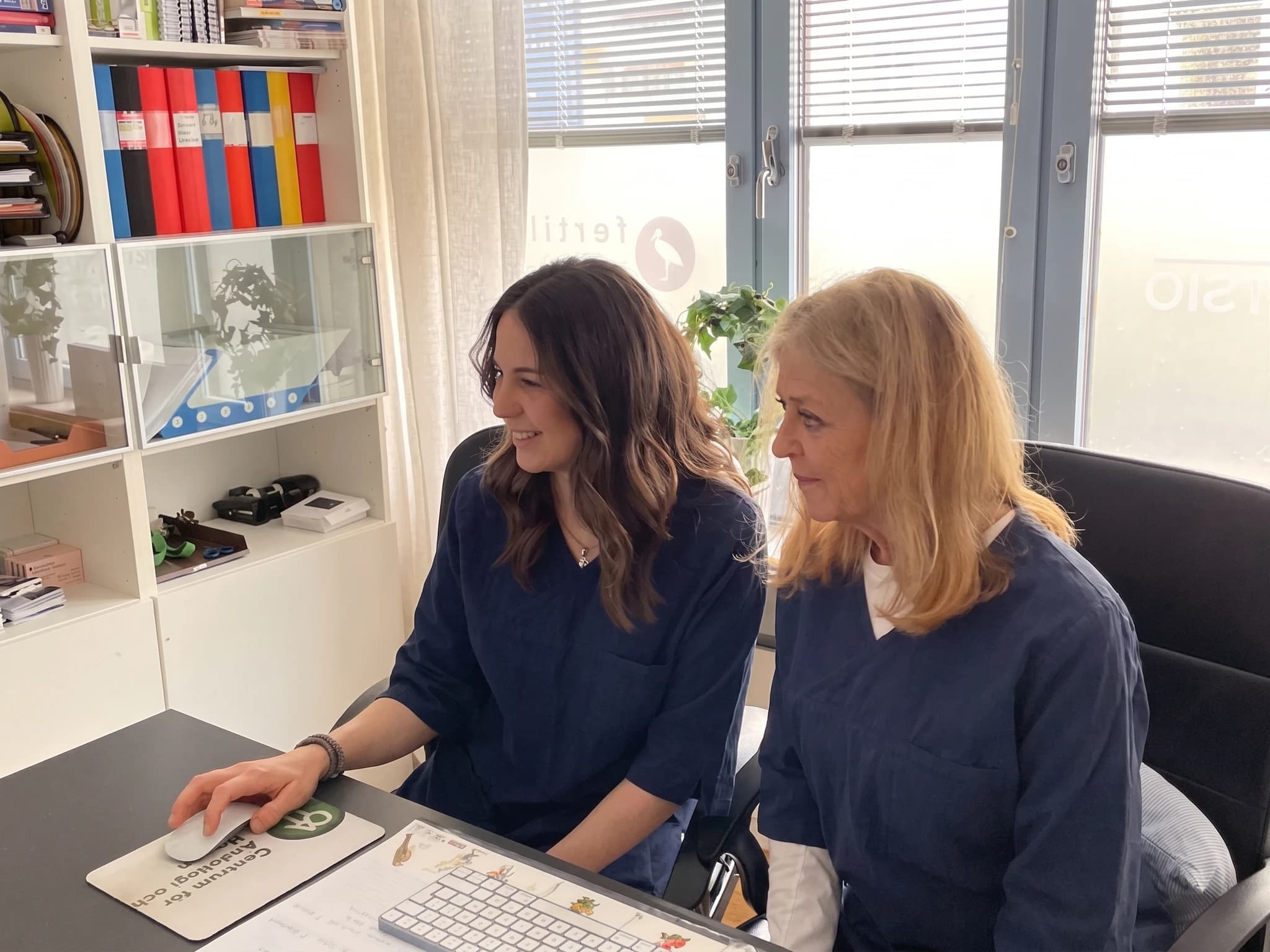 Två kvinnor sitter vid en dator och arbetar tillsammans på ett kontor.