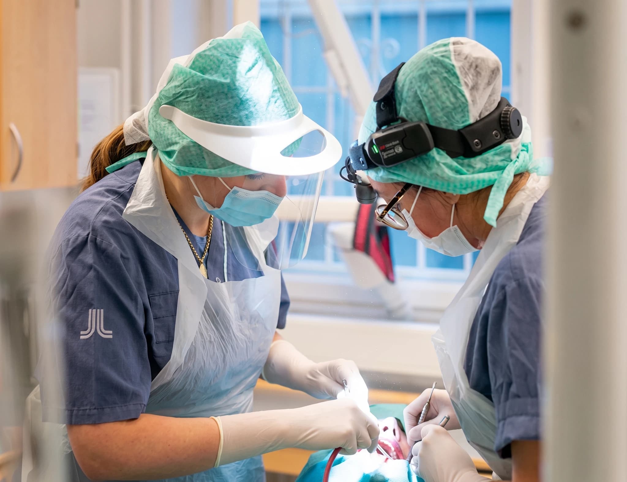 Två tandläkare i skyddsutrustning utför en tandoperation på en patient i en behandlingssal.