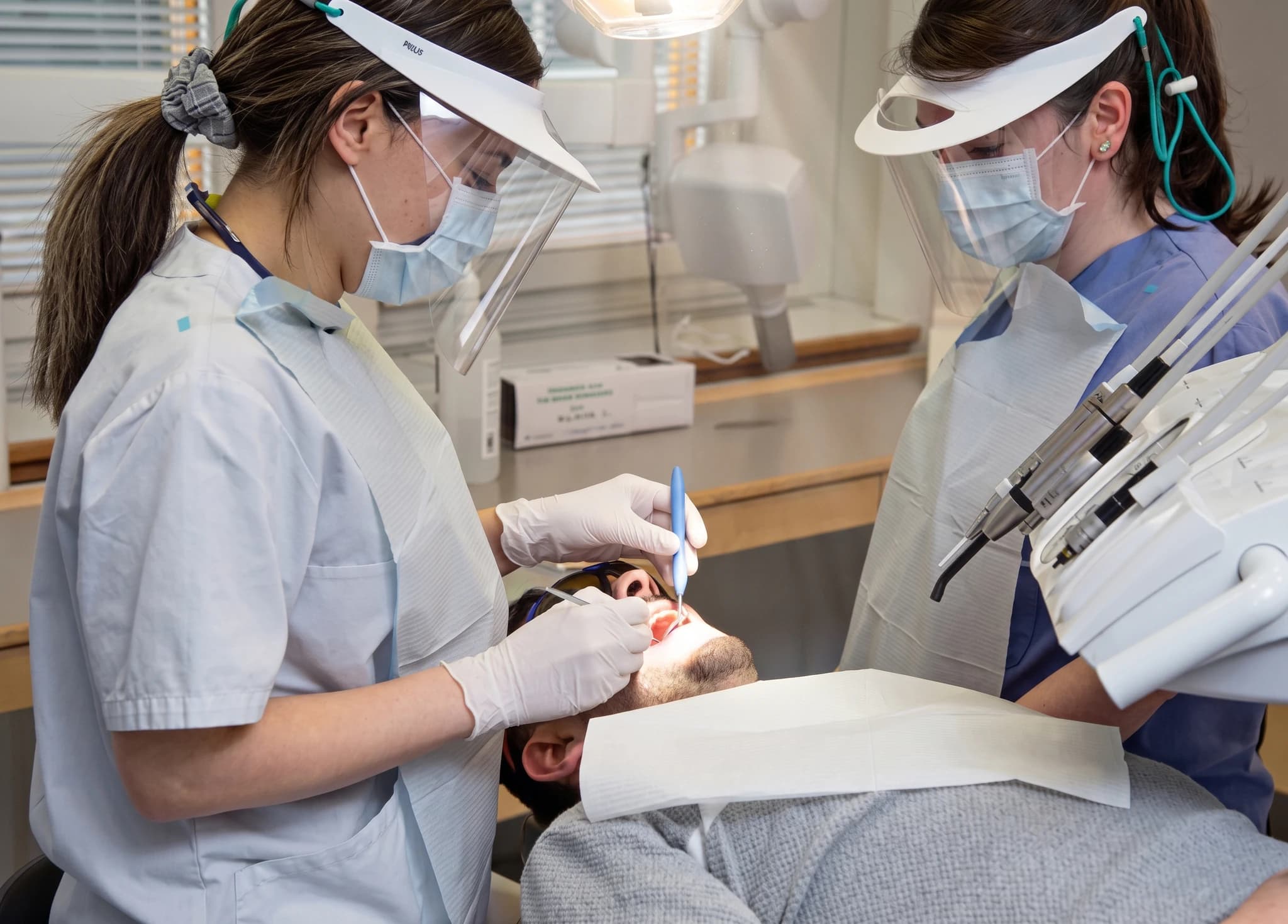 Tandläkare med skyddsutrustning undersöker en patients tänder med instrument på en tandläkarmottagning.