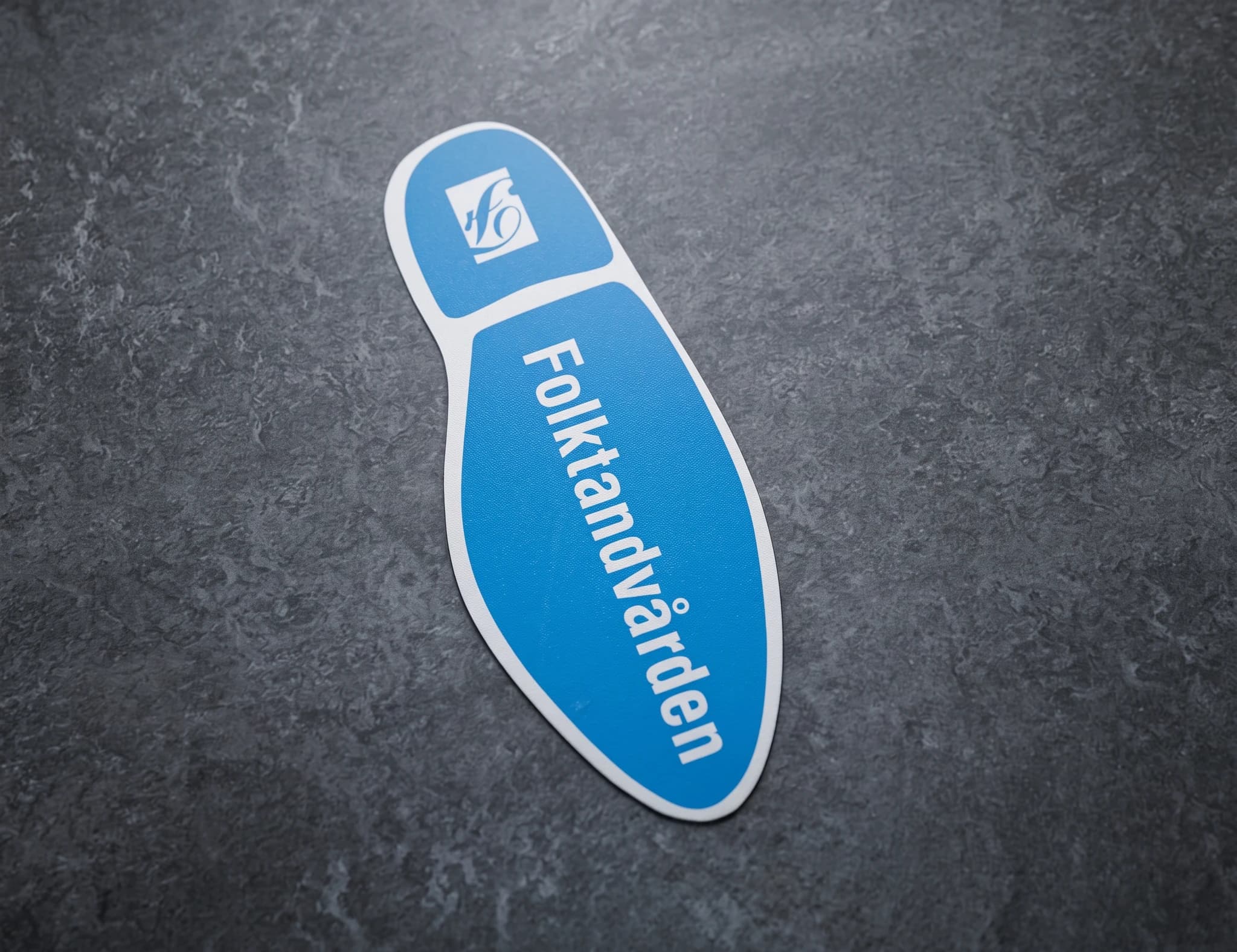 Folktandvårdens logotyp på en blå och vit fotavtrycksdekal.