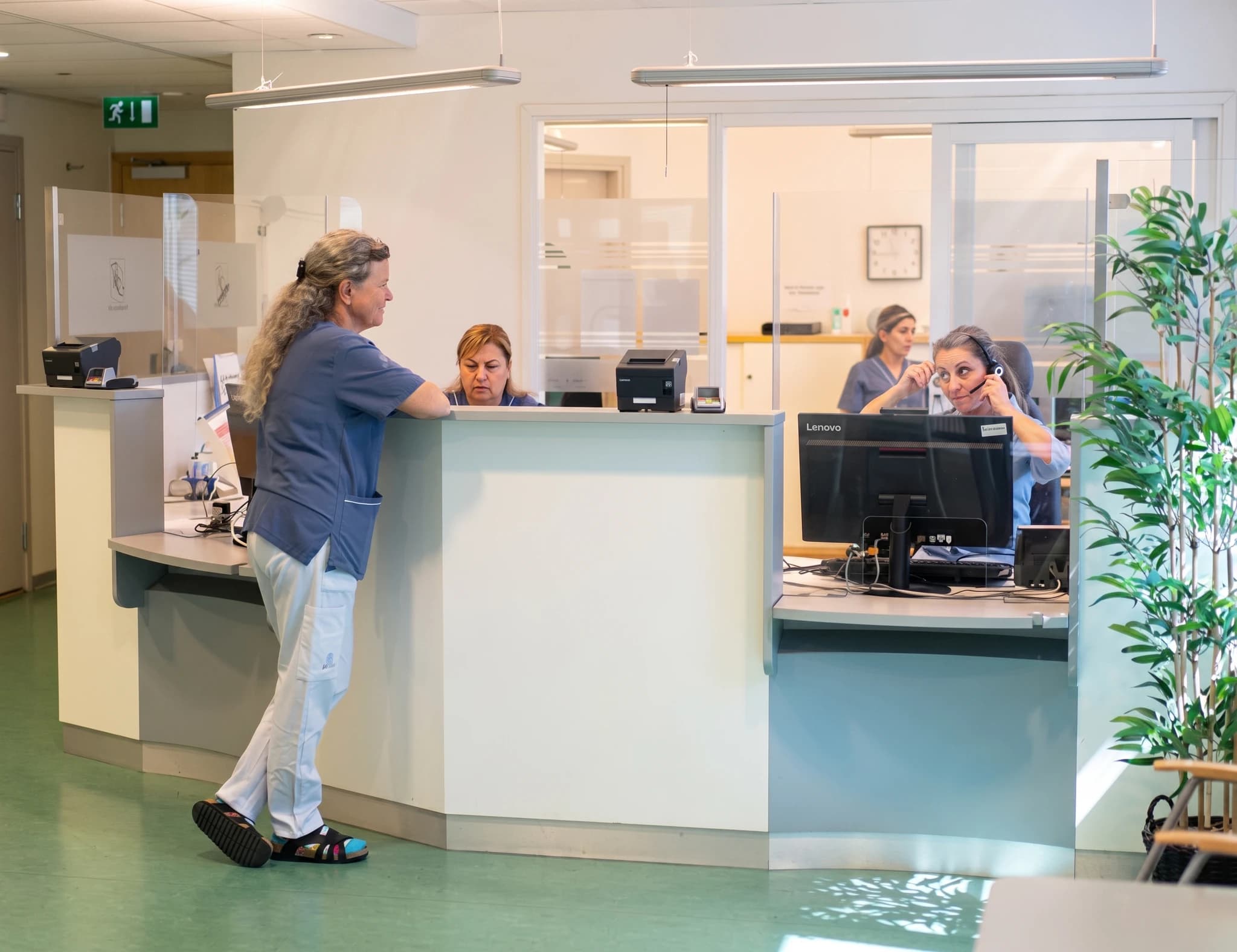 En receptionist med headset pratar i telefon vid en reception i en vårdcentral.