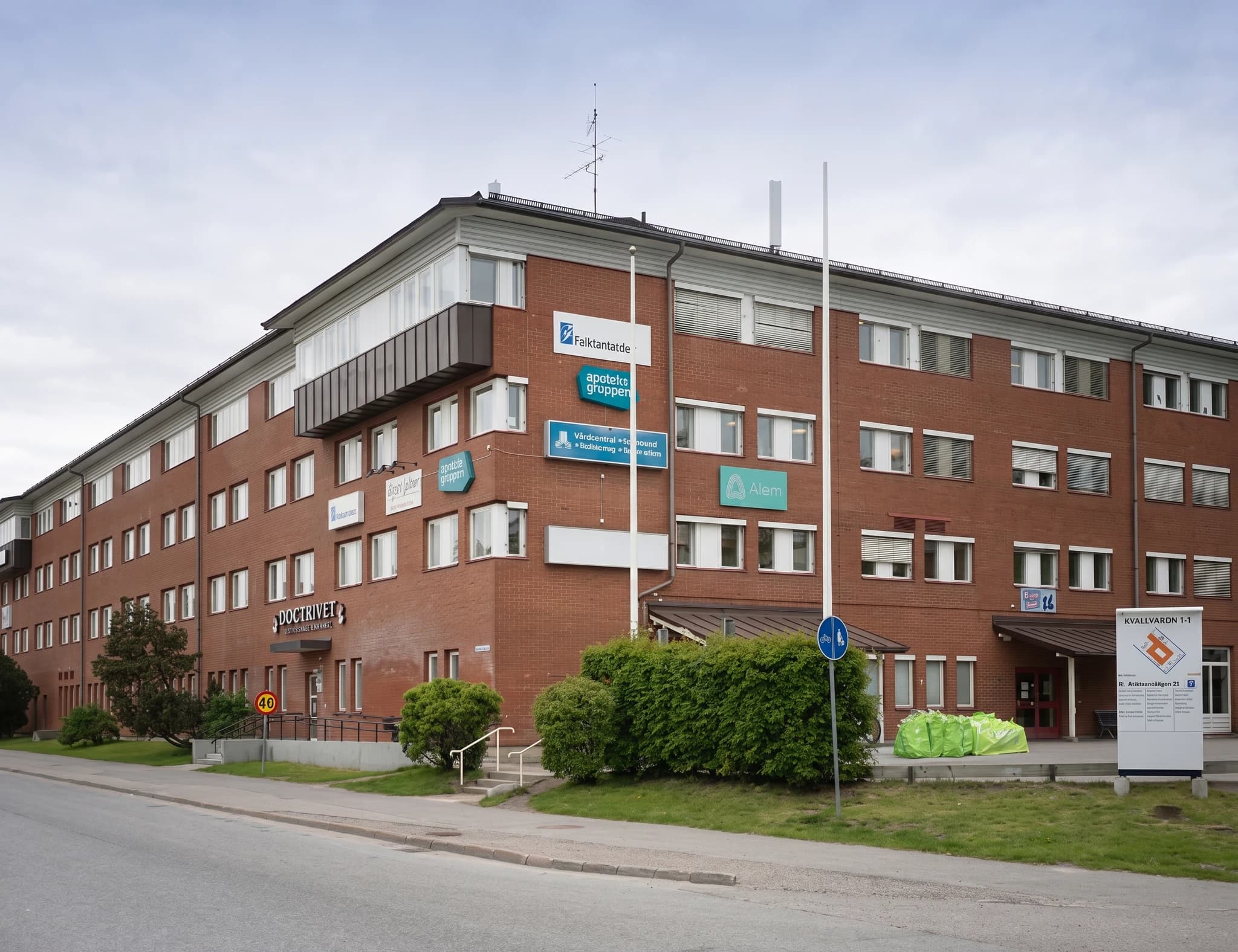 Exteriör av en tegelbyggnad med flera medicinska mottagningar, skyltar och gröna buskar.