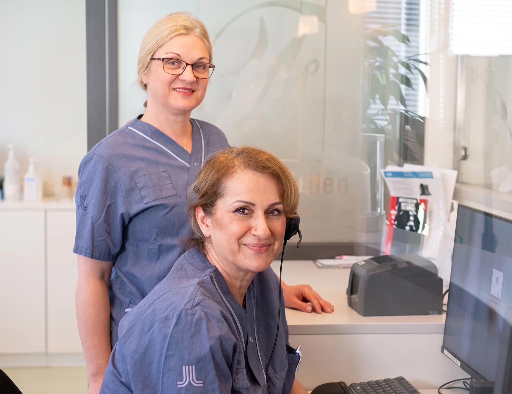 Två kvinnliga vårdpersonal ler vid receptionen på en klinik.