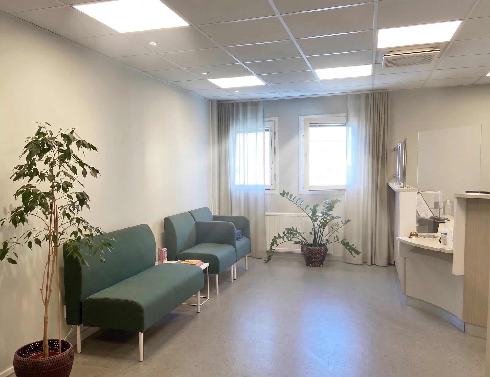 Ett väntrum med två gröna soffor, en stor grön växt och en reception i bakgrunden.