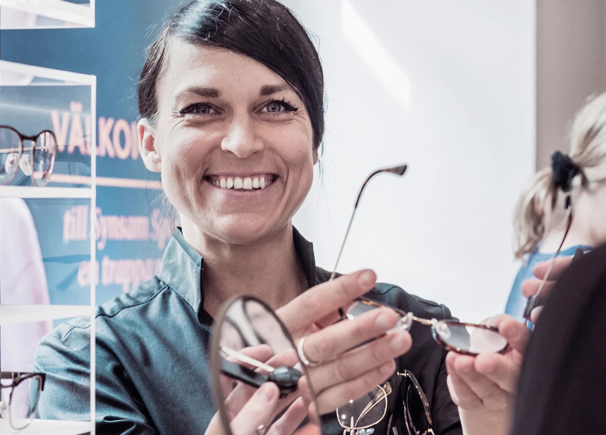 En optiker ler och håller upp ett par glasögon för en kund.