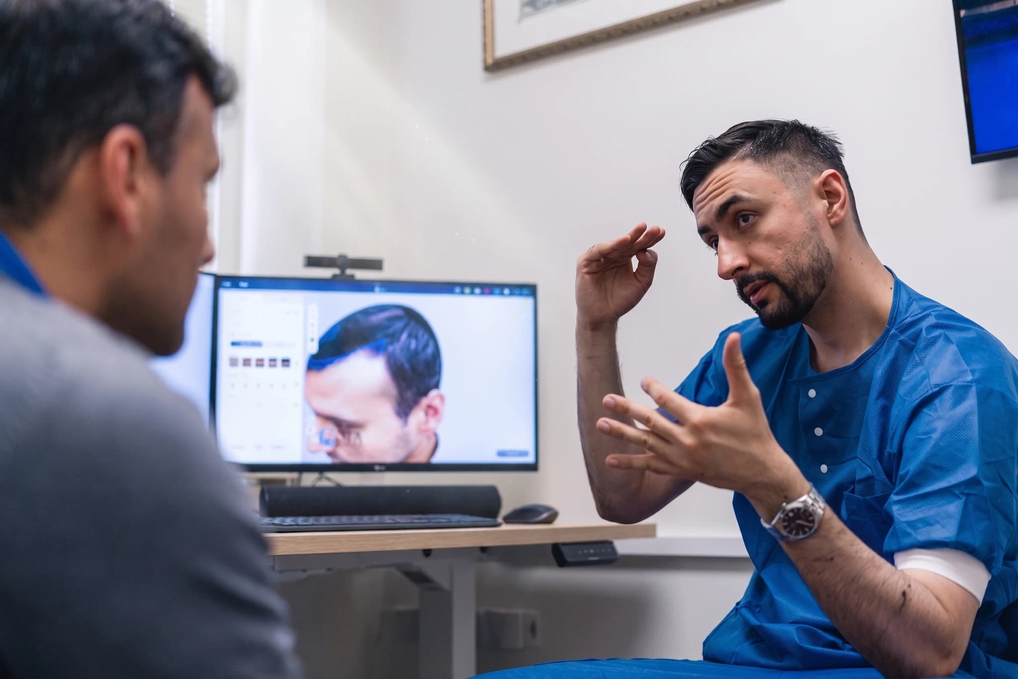 Läkare i blåa operationskläder gestikulerar medan han förklarar en bild av en patients hår för en annan person vid en datorskärm.