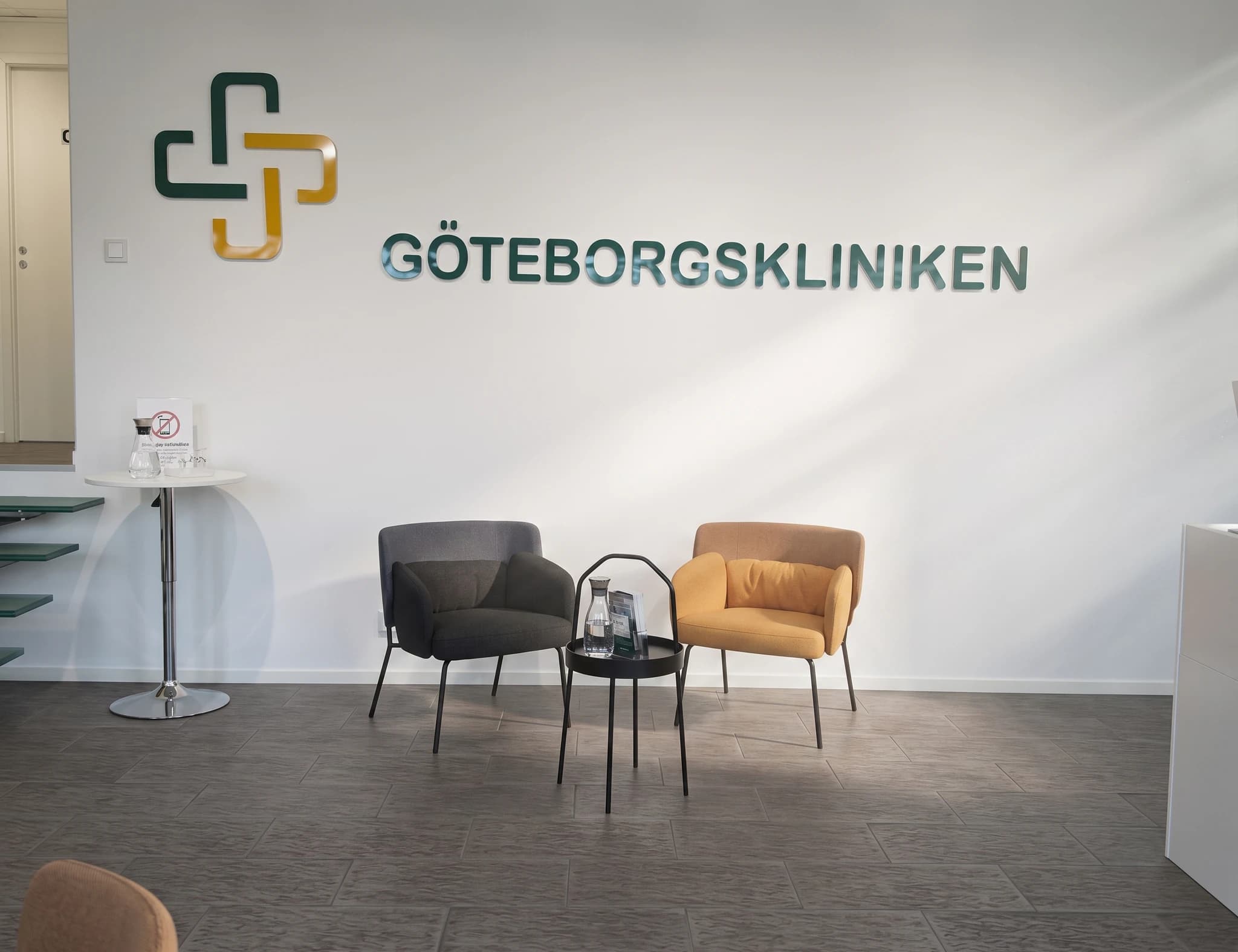 Väntrum med två fåtöljer, ett sidobord och företagets logotyp och namn på väggen.
