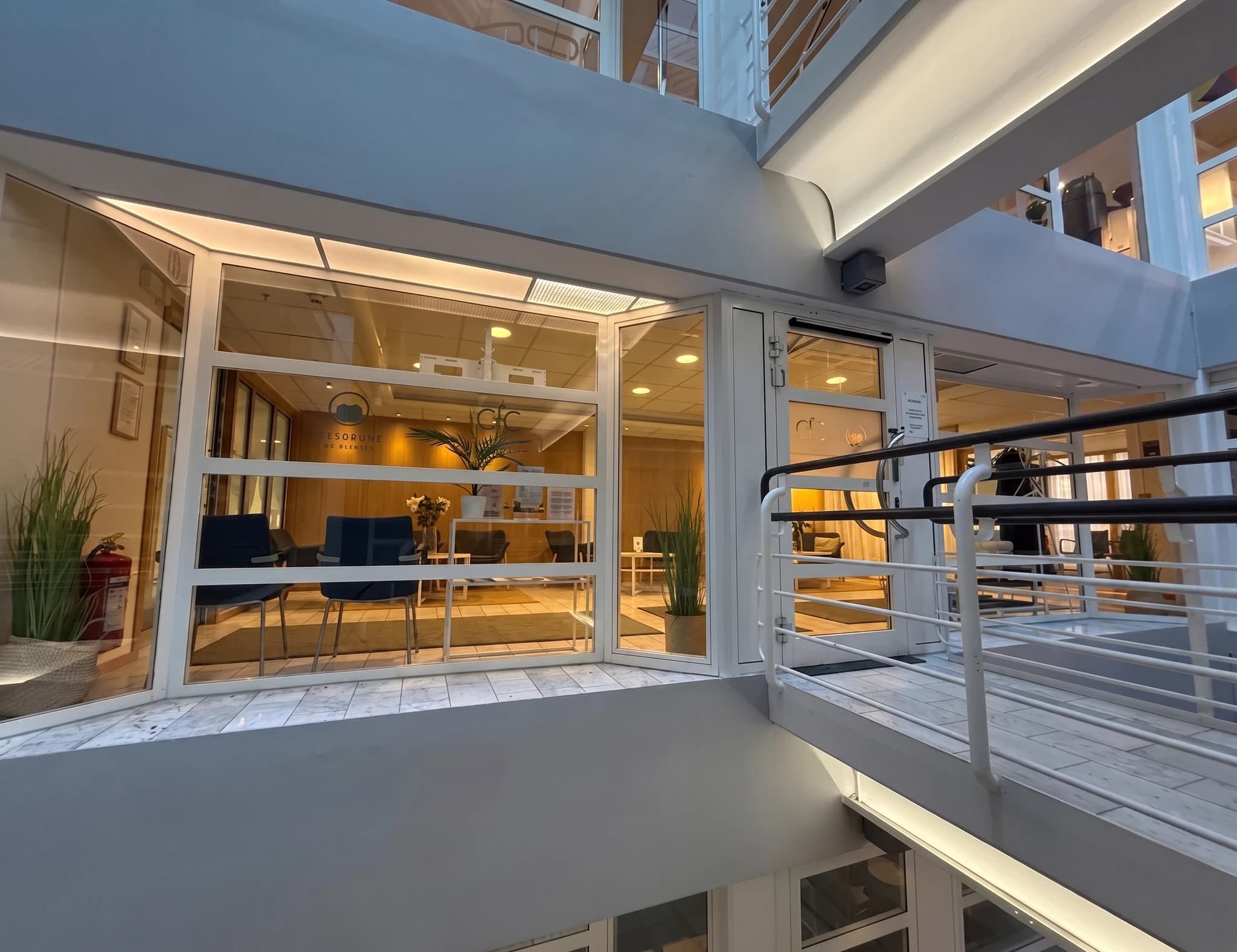 Reception med väntrumsstolar, växter och fönster mot ett atrium.