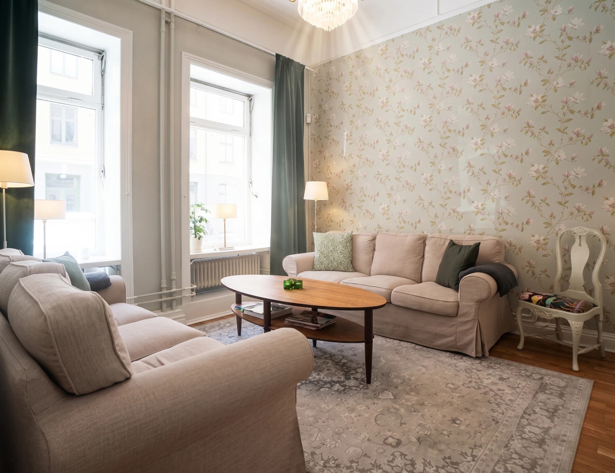 Vardagsrum med blommig tapet, beige soffa, soffbord och matta.