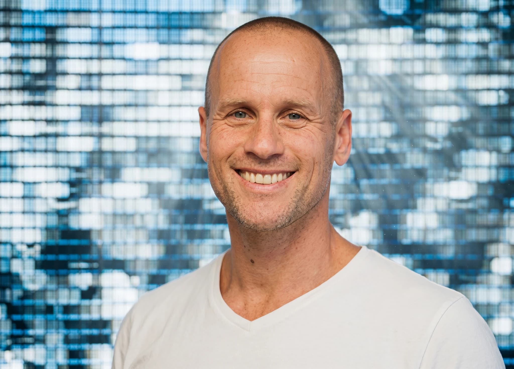 En medelålders man med rakad skalle ler mot kameran i en studiofotografering.