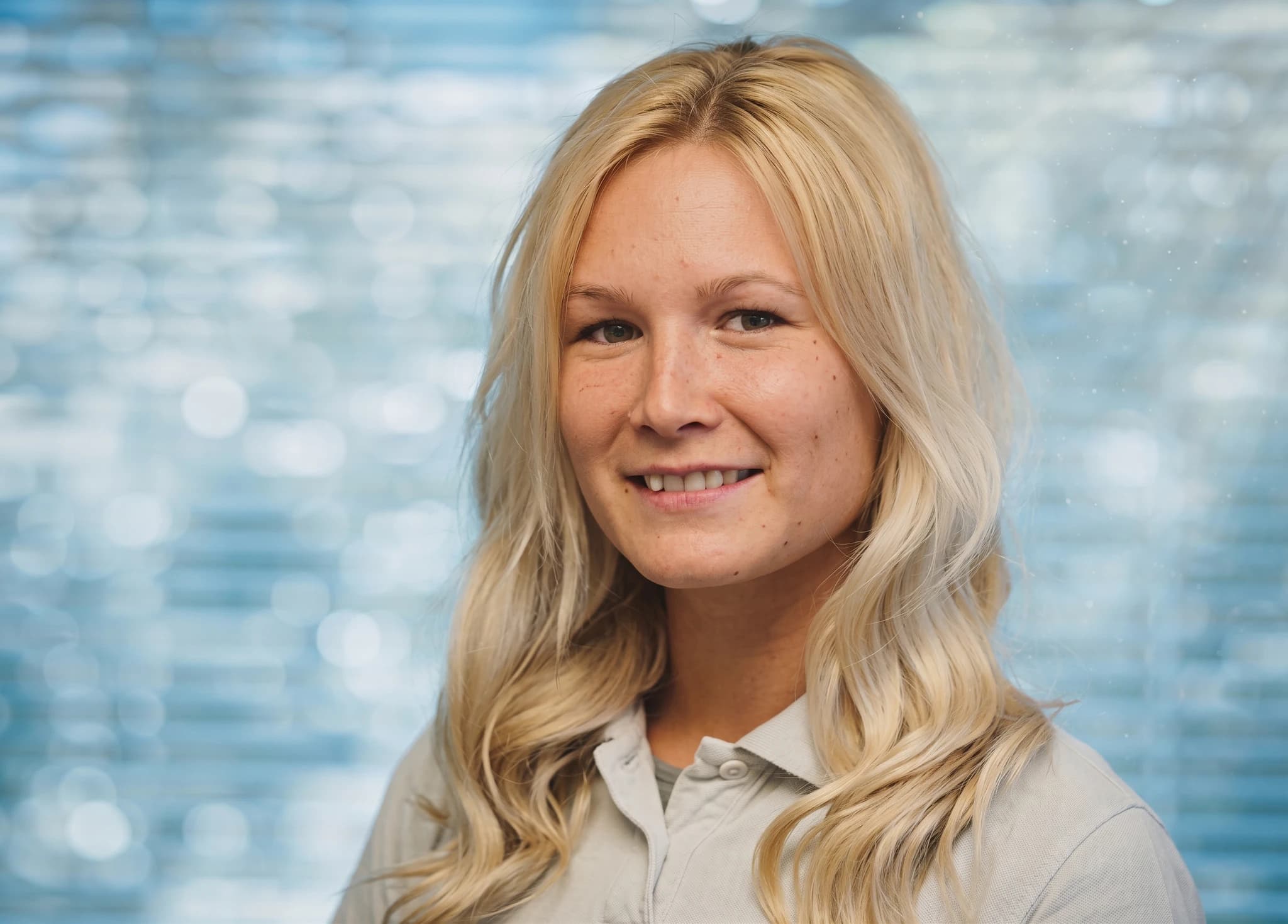 En kvinna med blont hår ler mot kameran i en studiofotografering.