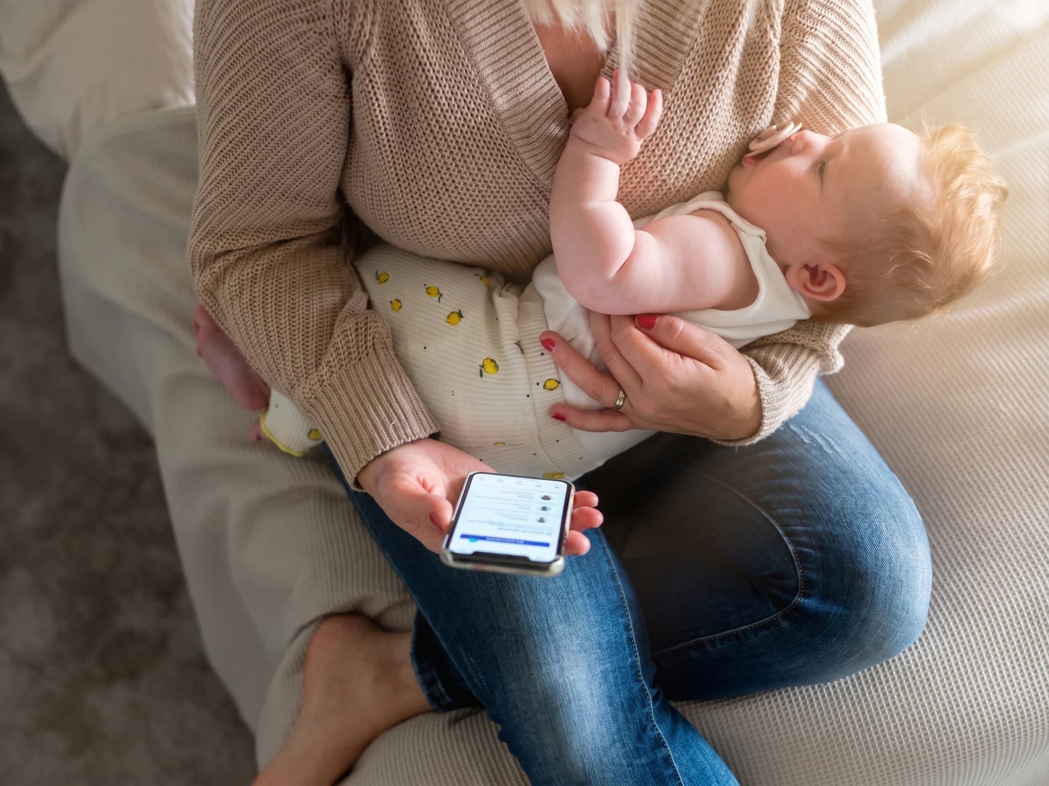 En mamma sitter med sin baby i famnen och tittar på sin mobiltelefon.