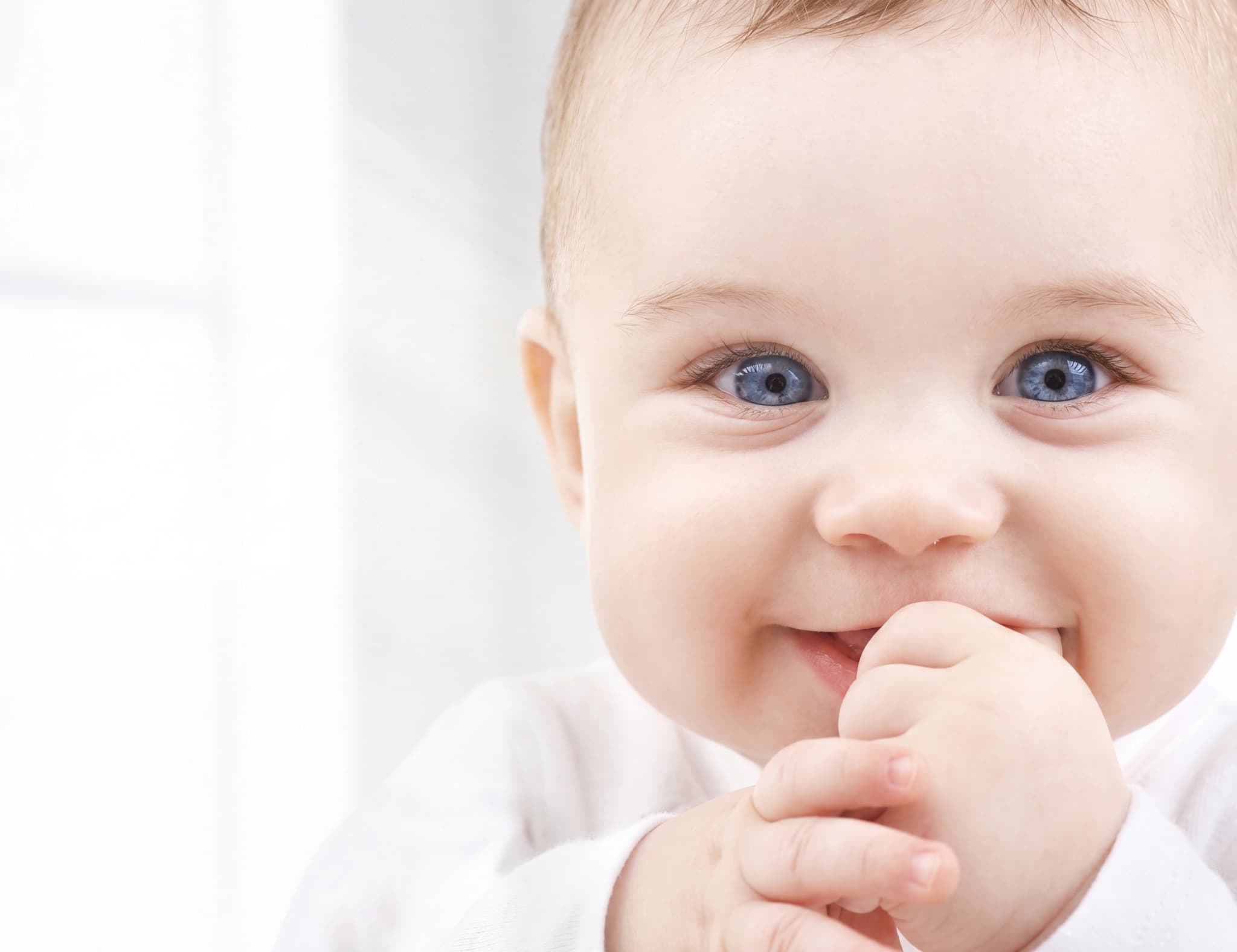En närbild på en baby med blå ögon som tuggar på sina fingrar.
