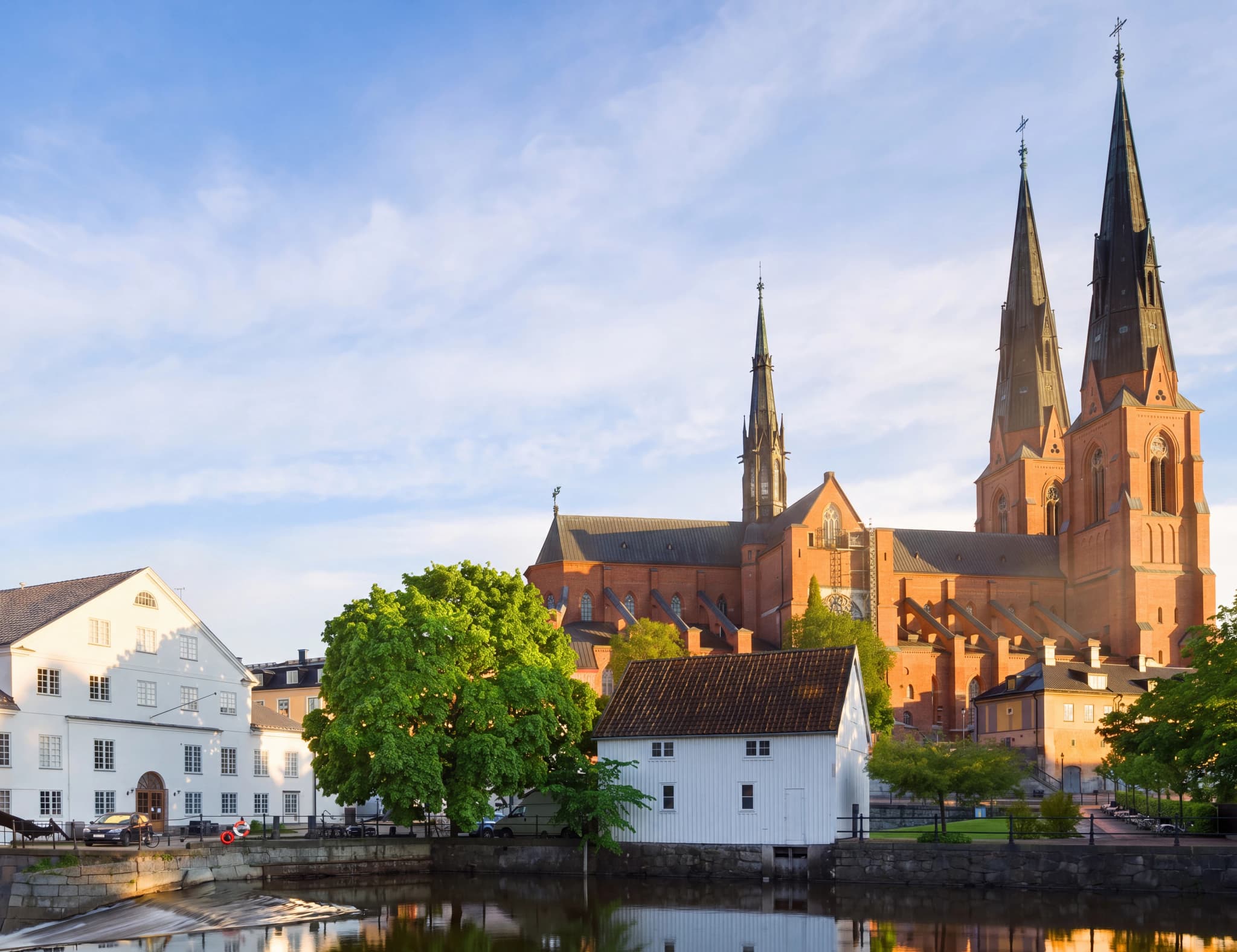 Uppsala domkyrka och historiska byggnader längs Fyrisån en solig dag.