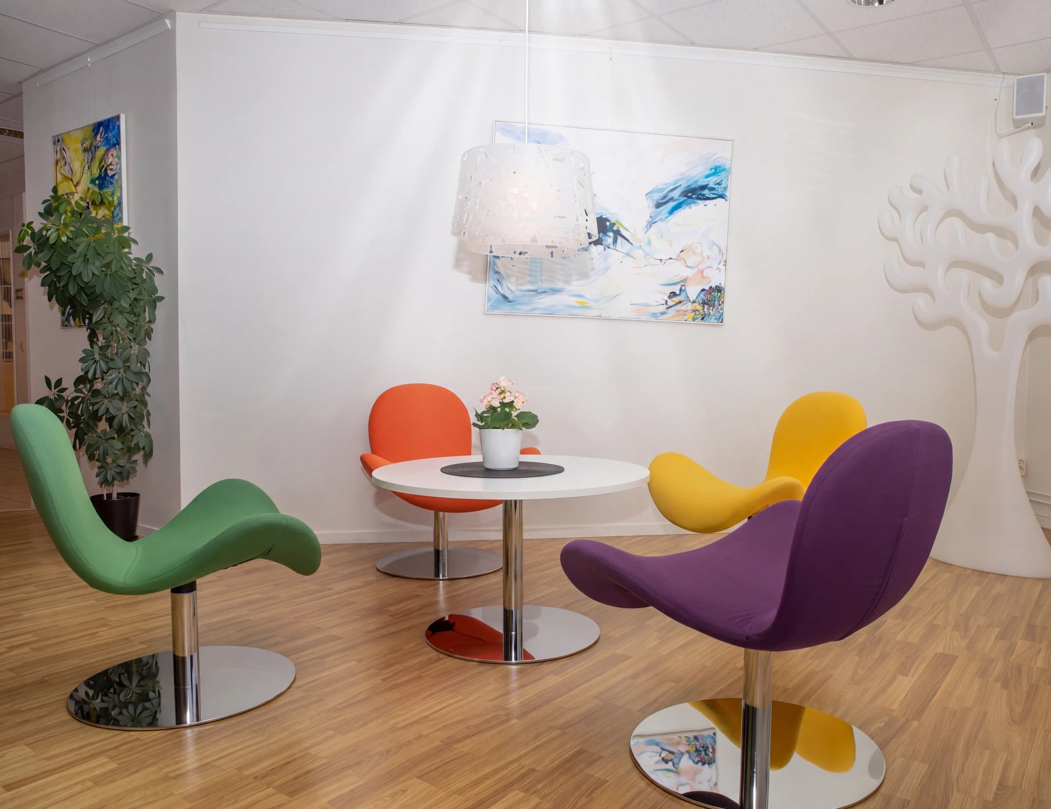 En modern väntrumsmiljö med en vit rund disk, olika färgglada fåtöljer och en stor vit träliknande dekoration på väggen.