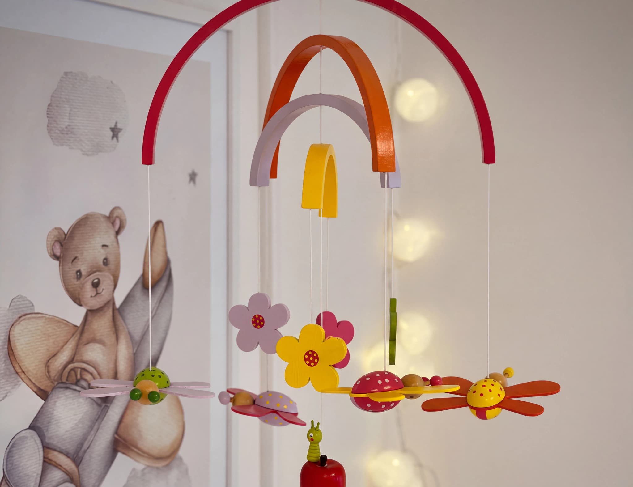 En mobil för babyrummet med träleksaker i form av insekter och blommor, hängande från en båge.