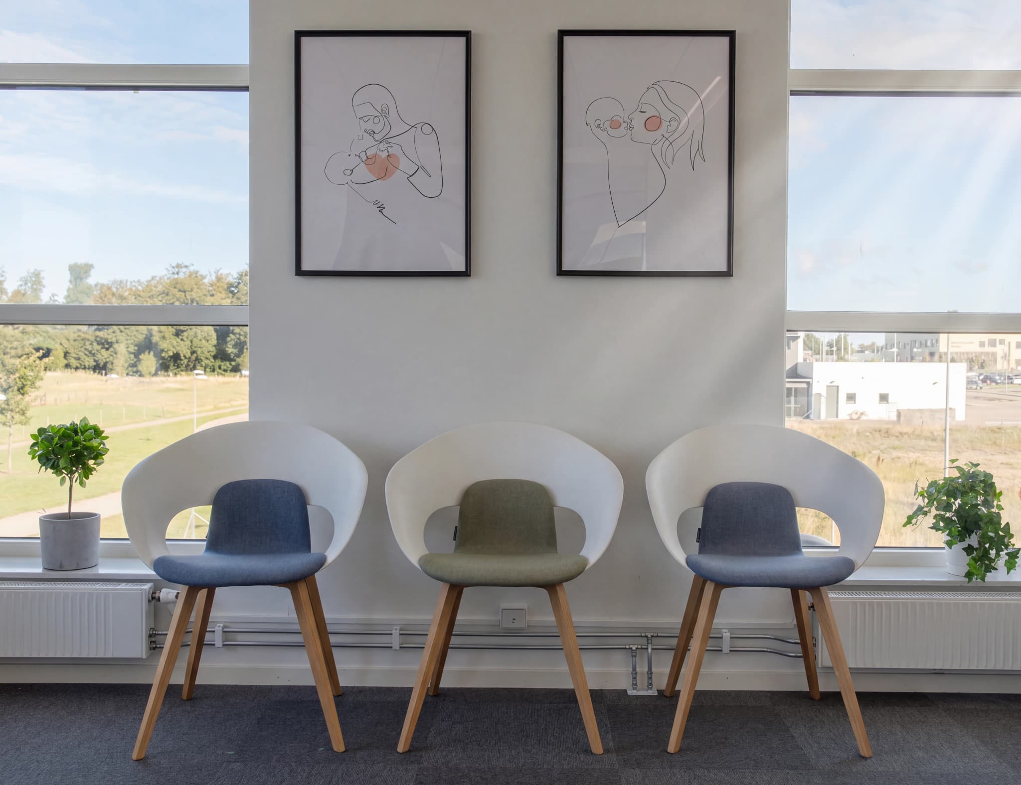 Väntrum med tre moderna stolar och stora fönster med utsikt över en grönskande omgivning.