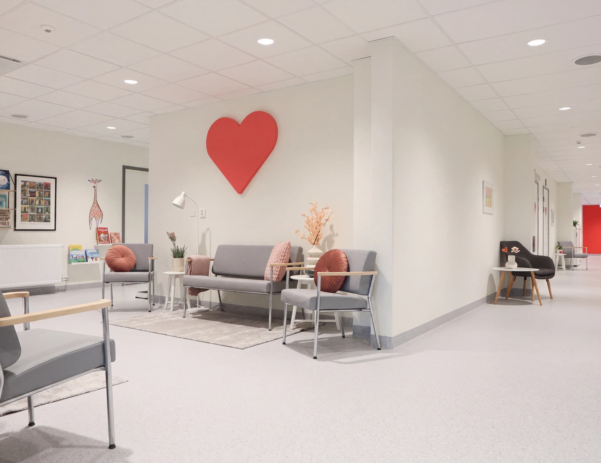 Modern väntrumsmiljö på en klinik med gråa möbler, ett stort rött hjärta på väggen och konst på väggarna.