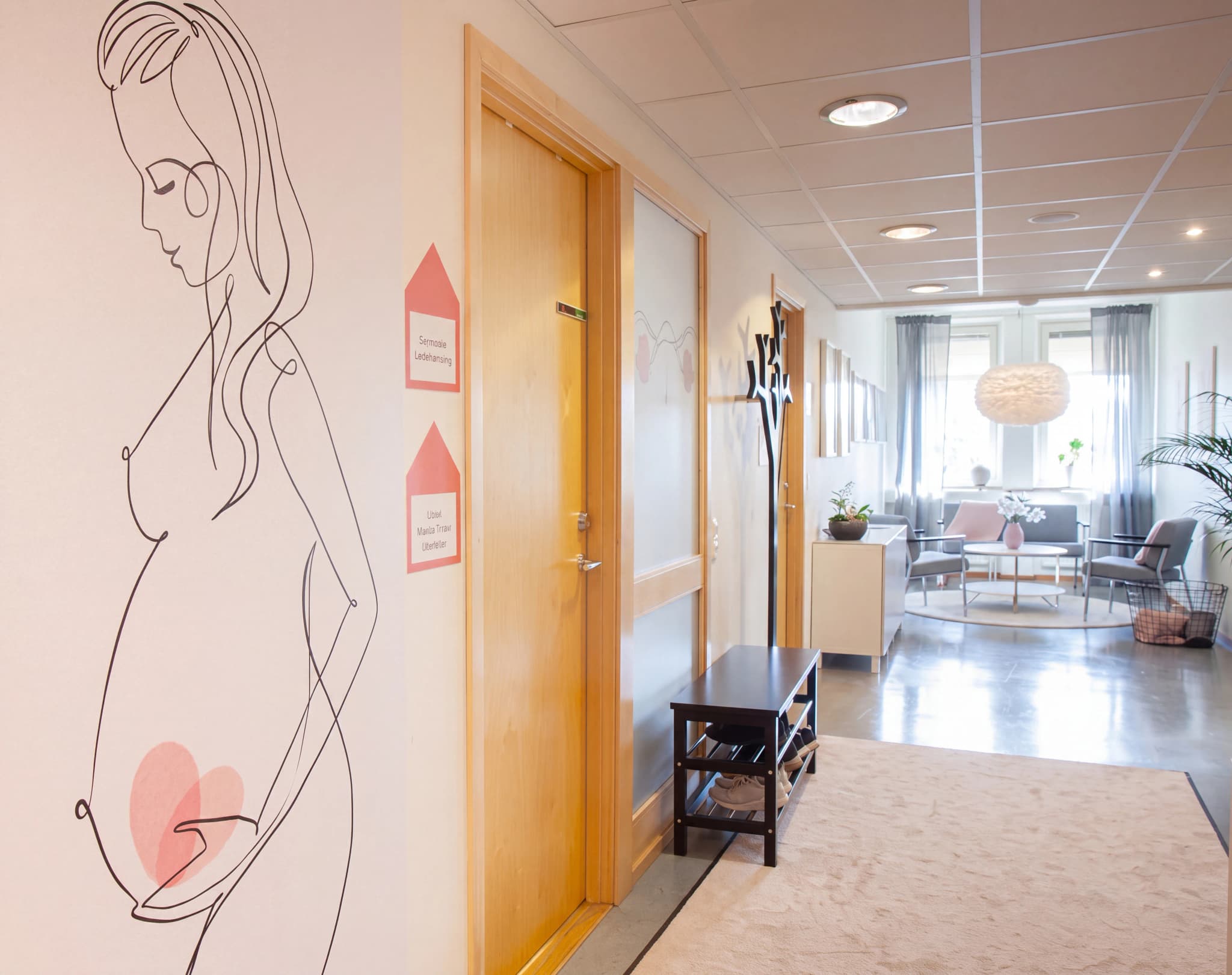 En hall med konst av en gravid kvinna på väggen, en dörr och en väntmöbel med soffa och bord i bakgrunden.
