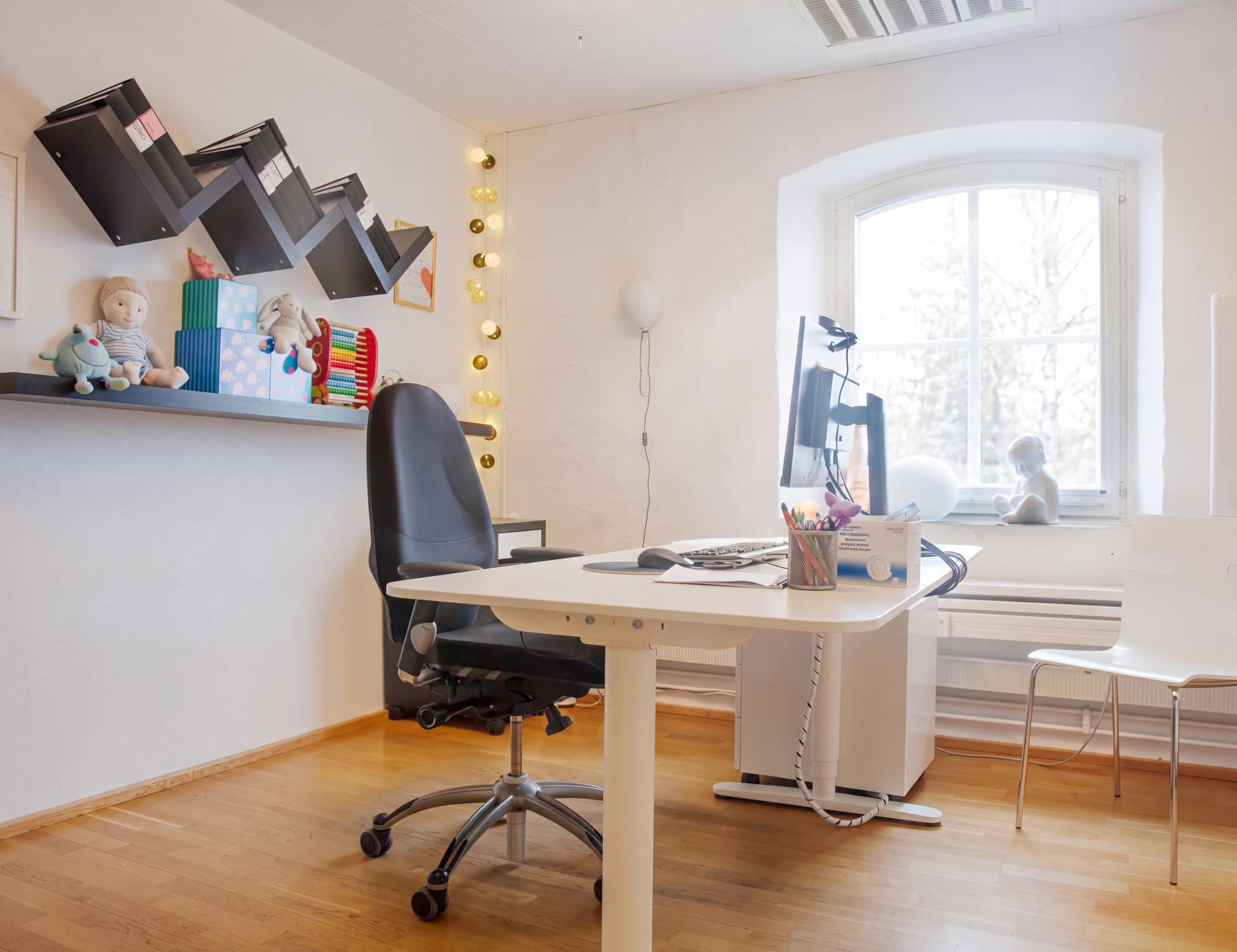 Ett modernt höj- och sänkbart skrivbord med en ergonomisk kontorsstol framför ett stort fönster i ett ljust rum.